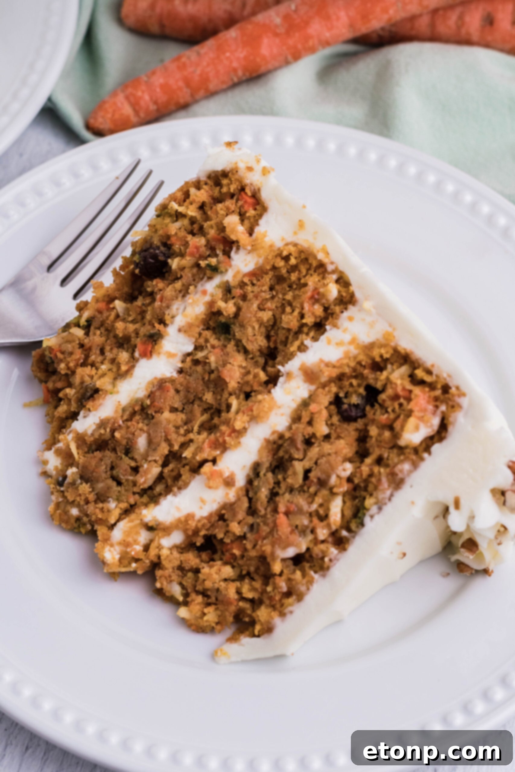 A whole carrot cake on a white cake stand with a single slice neatly placed on a white plate next to it, inviting a taste.