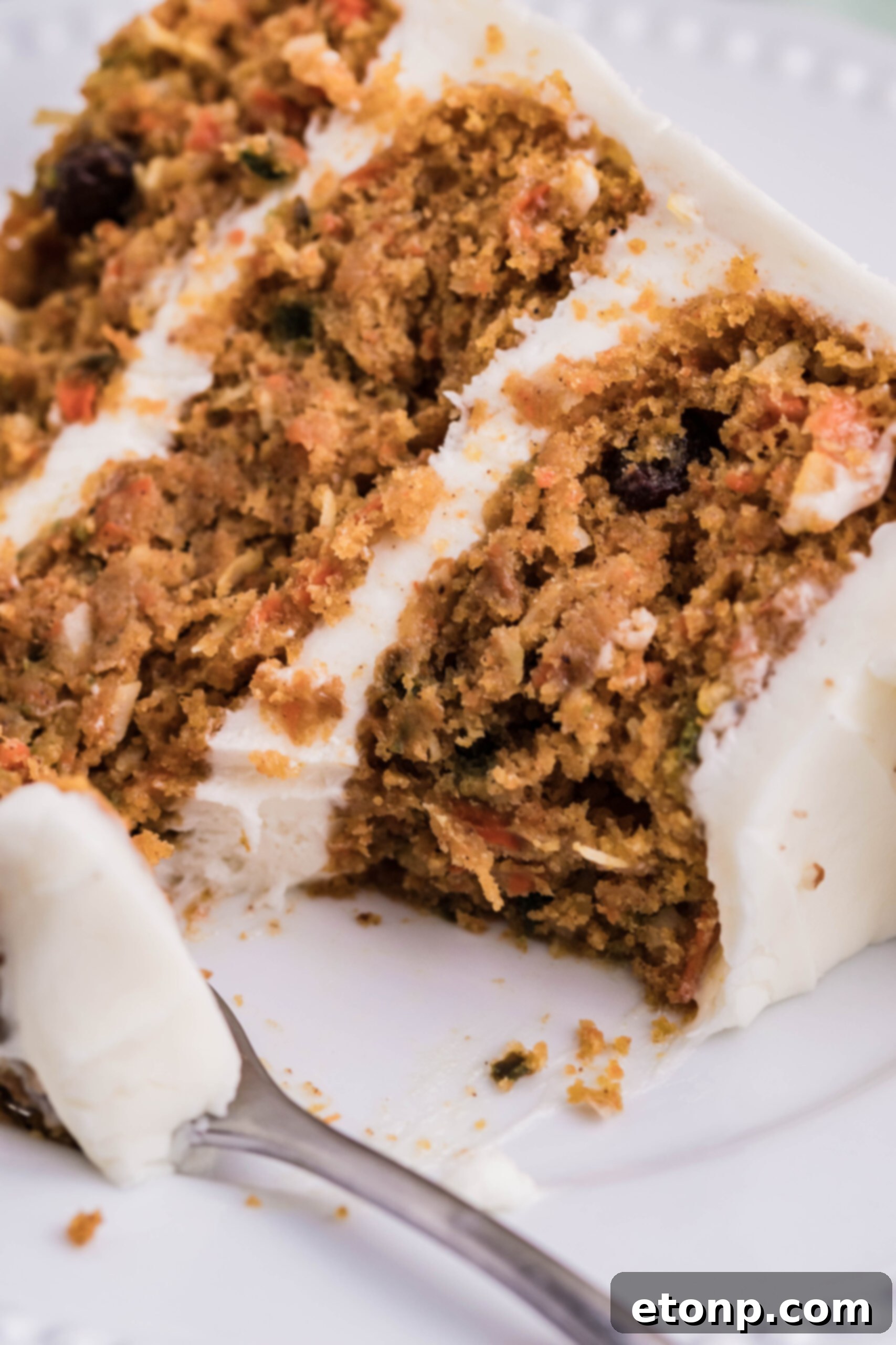 A close-up of a slice of carrot cake on a white plate, with a small bite taken out, revealing the moist layers and rich frosting.