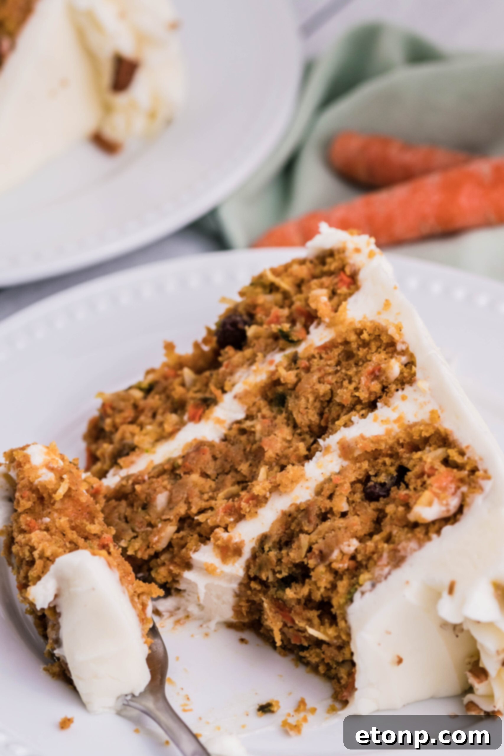 An even closer view of a slice of carrot cake on a white plate, with a larger bite removed, emphasizing the cake's moistness and delicate crumb.