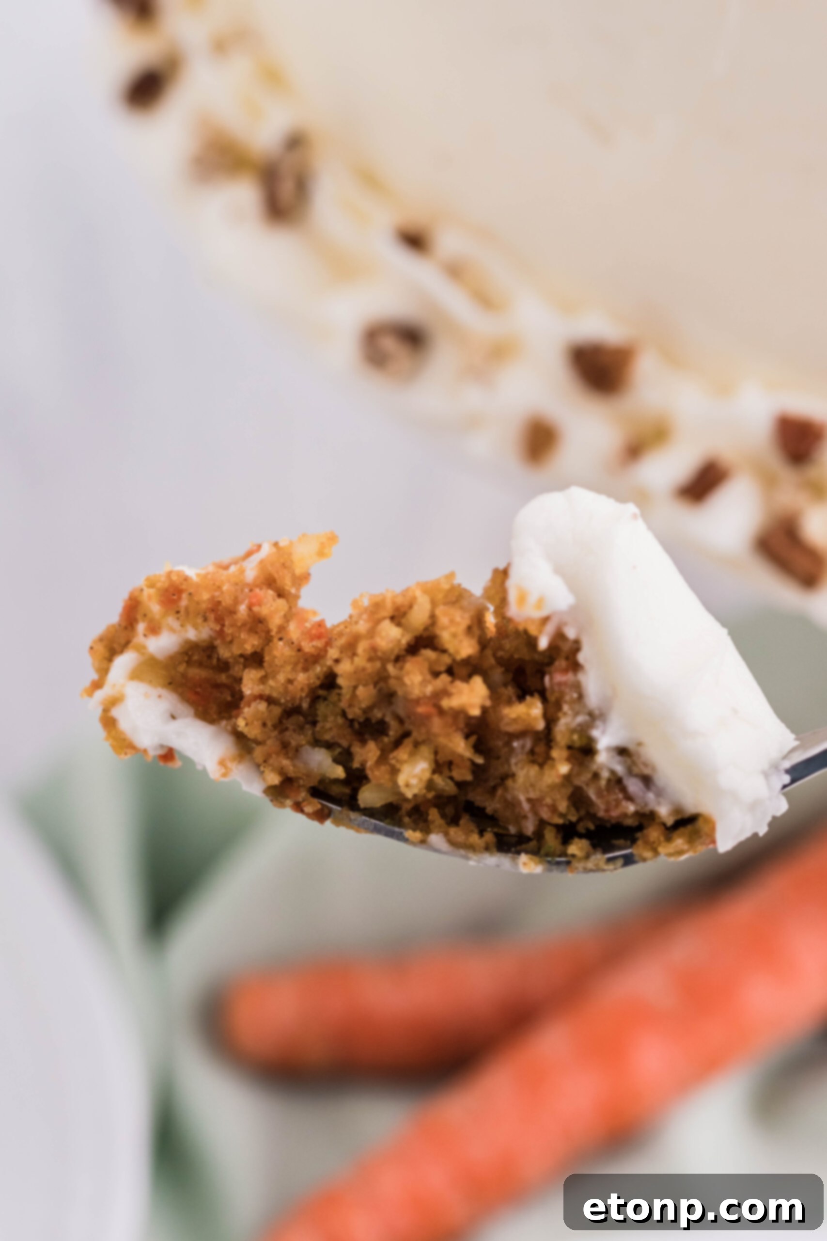 A side view of a perfect bite of carrot cake on a silver fork, ready to be enjoyed, showing the distinct layers of cake and frosting.