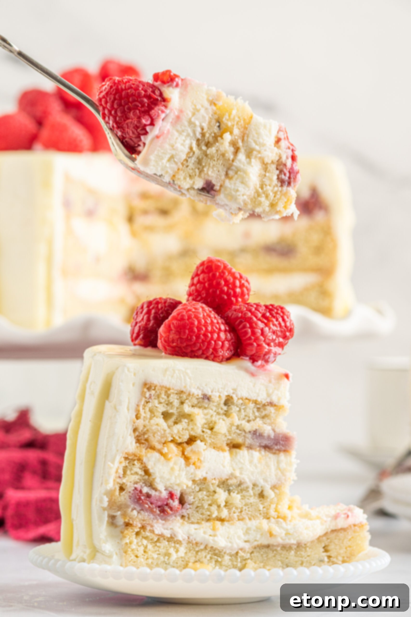 Side view of a bite of White Chocolate Cake with Raspberries on a silver fork.