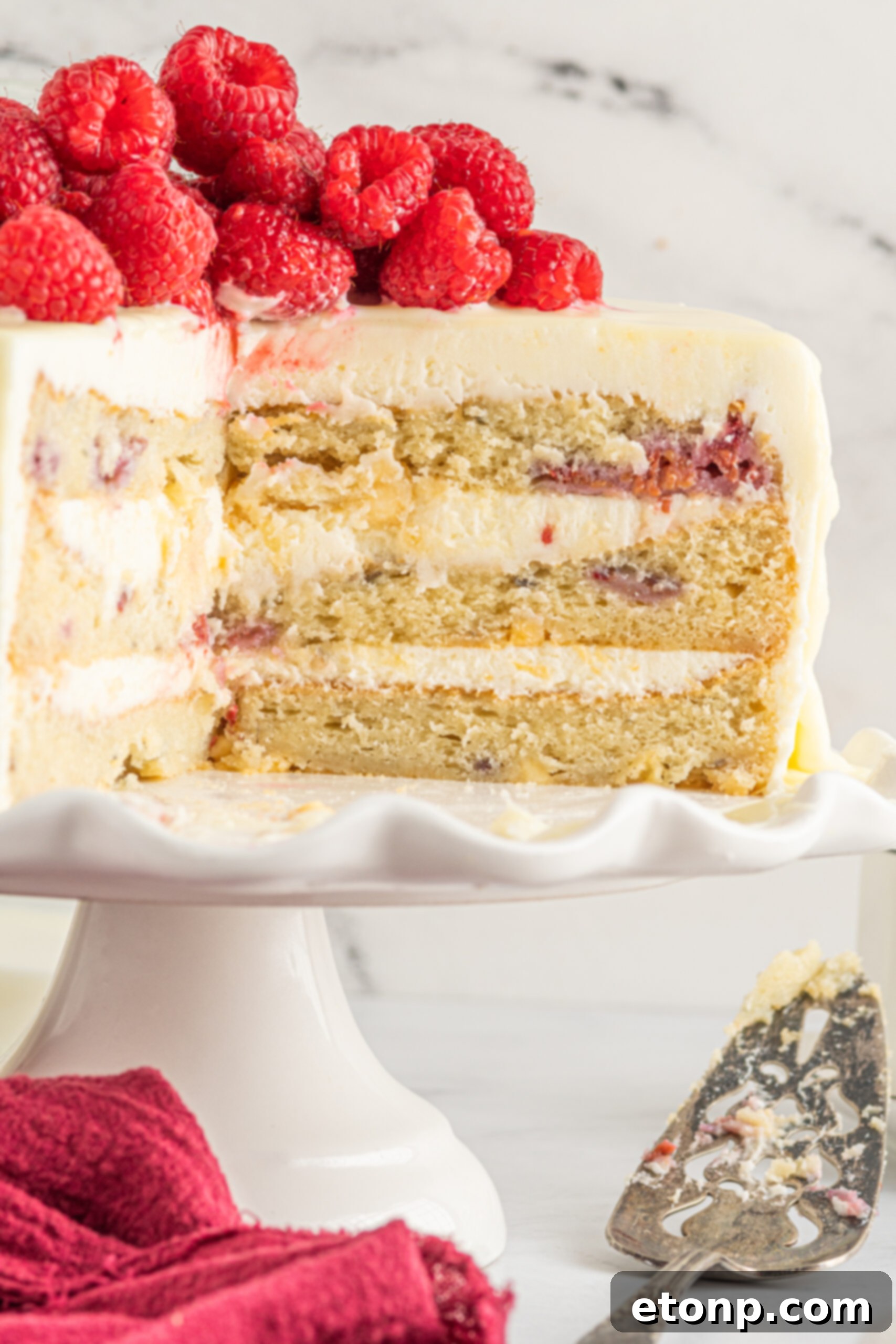 Front view of White Chocolate Cake with Raspberries on a white cake stand.