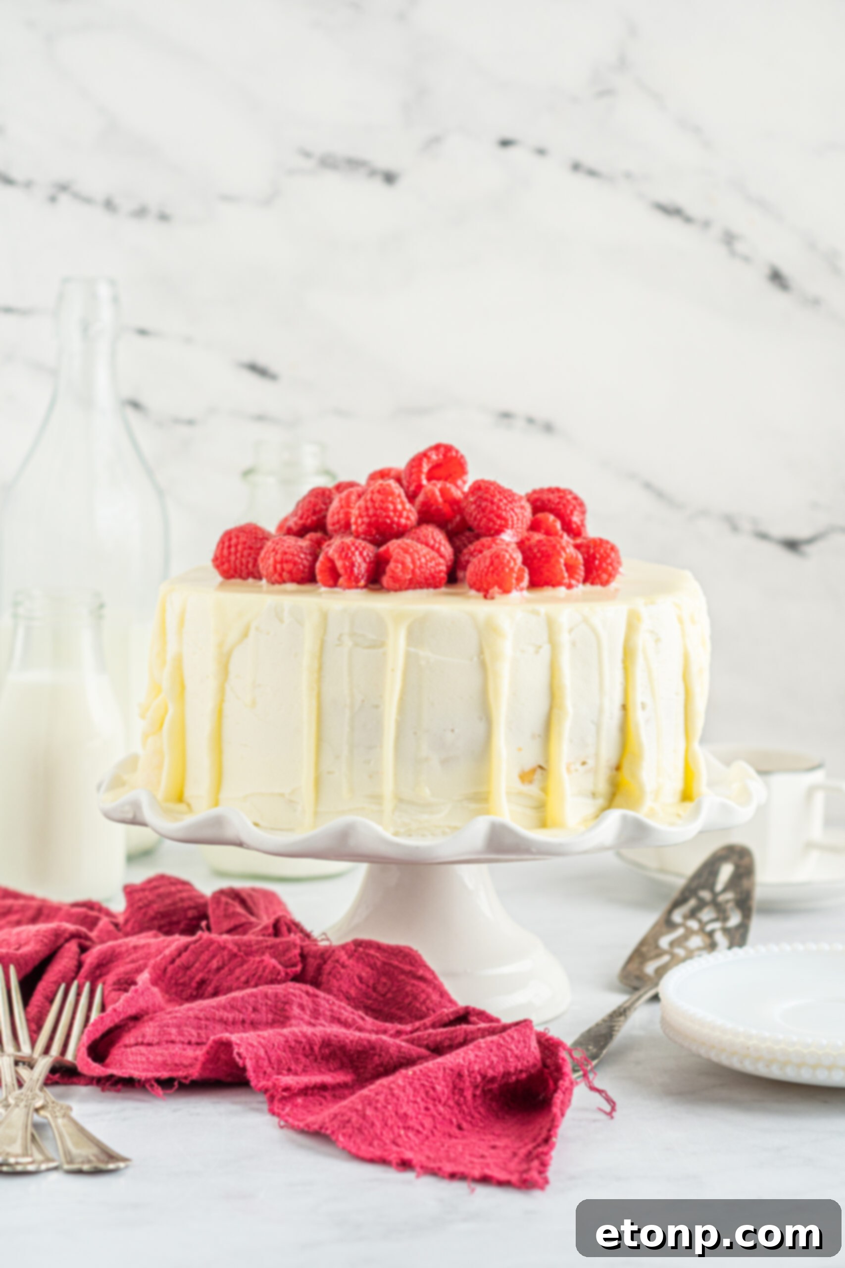 Front view of White Chocolate Cake with Raspberries on a white cake stand.