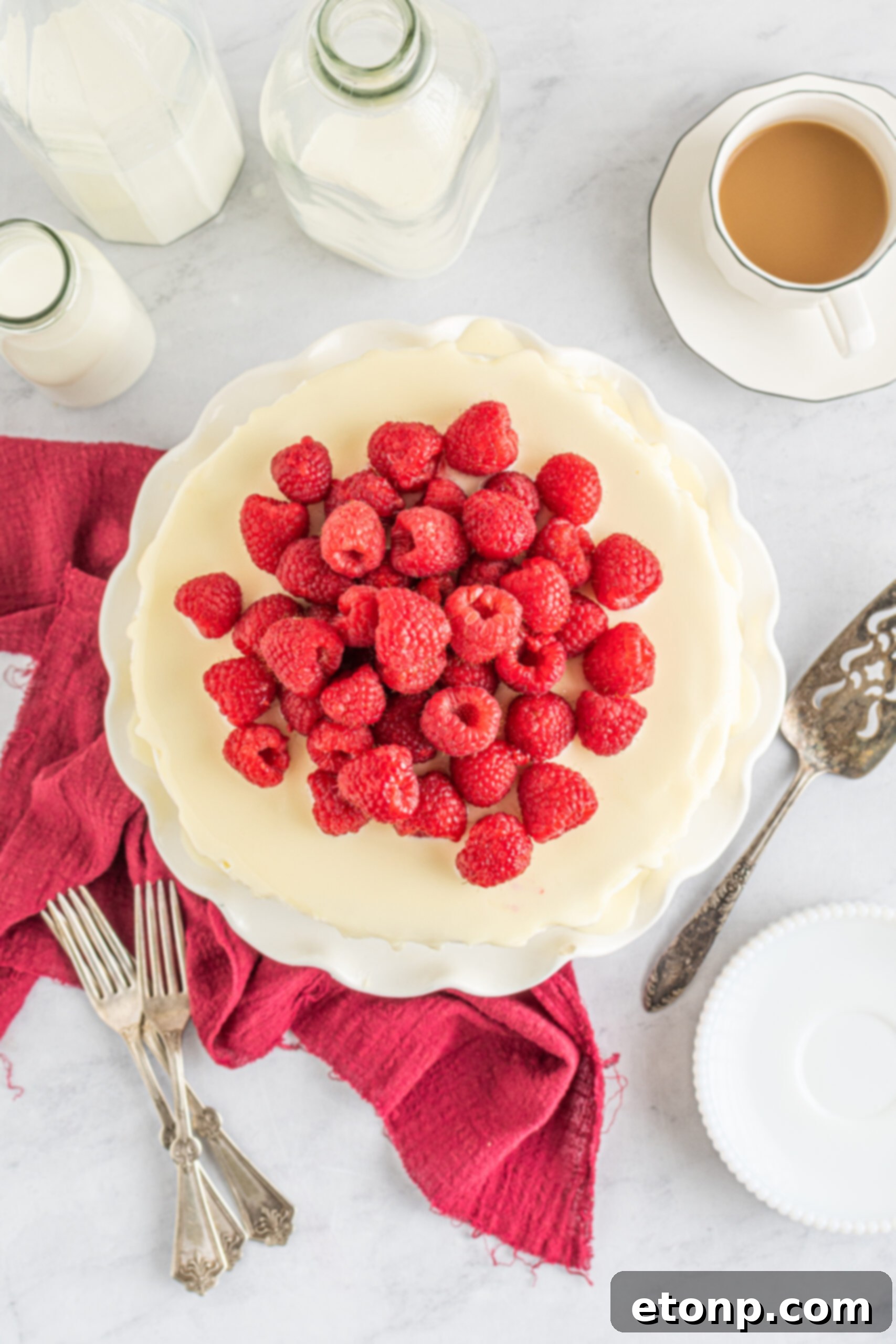 Overhead view of White Chocolate Cake with Raspberries on a white cake stand.