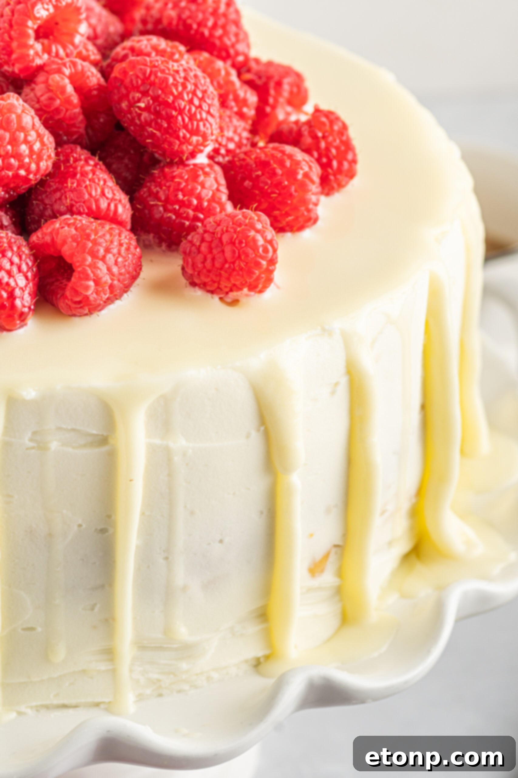 Up close view of White Chocolate Cake with Raspberries on a white cake stand.
