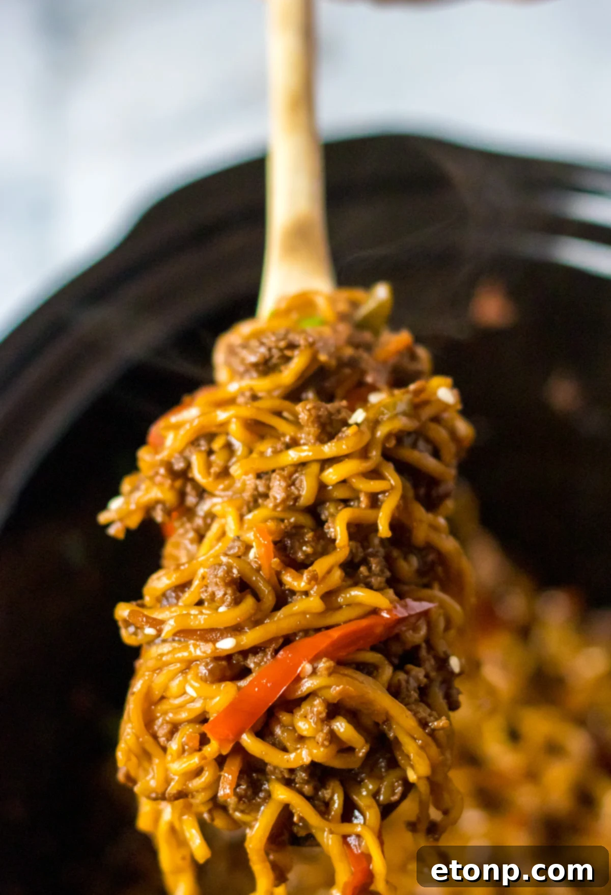 Hearty Slow Cooked Beef Ramen 10 Close up view of Slow Cooker Beef Ramen in a crock pot with a wooden spoon removing a serving.