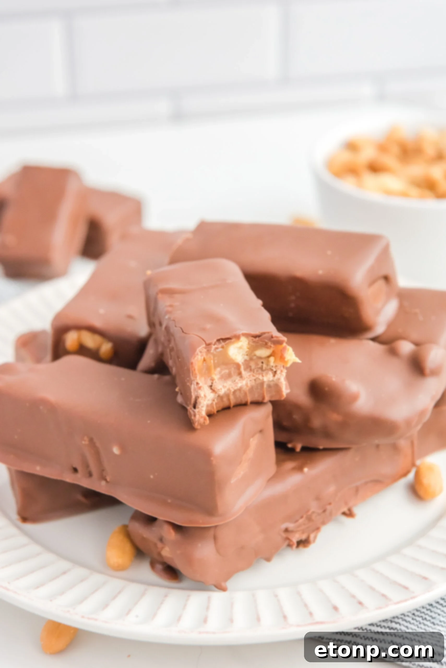 Homemade Snickers Candy Bars piled on a white serving plate with a bite missing from one