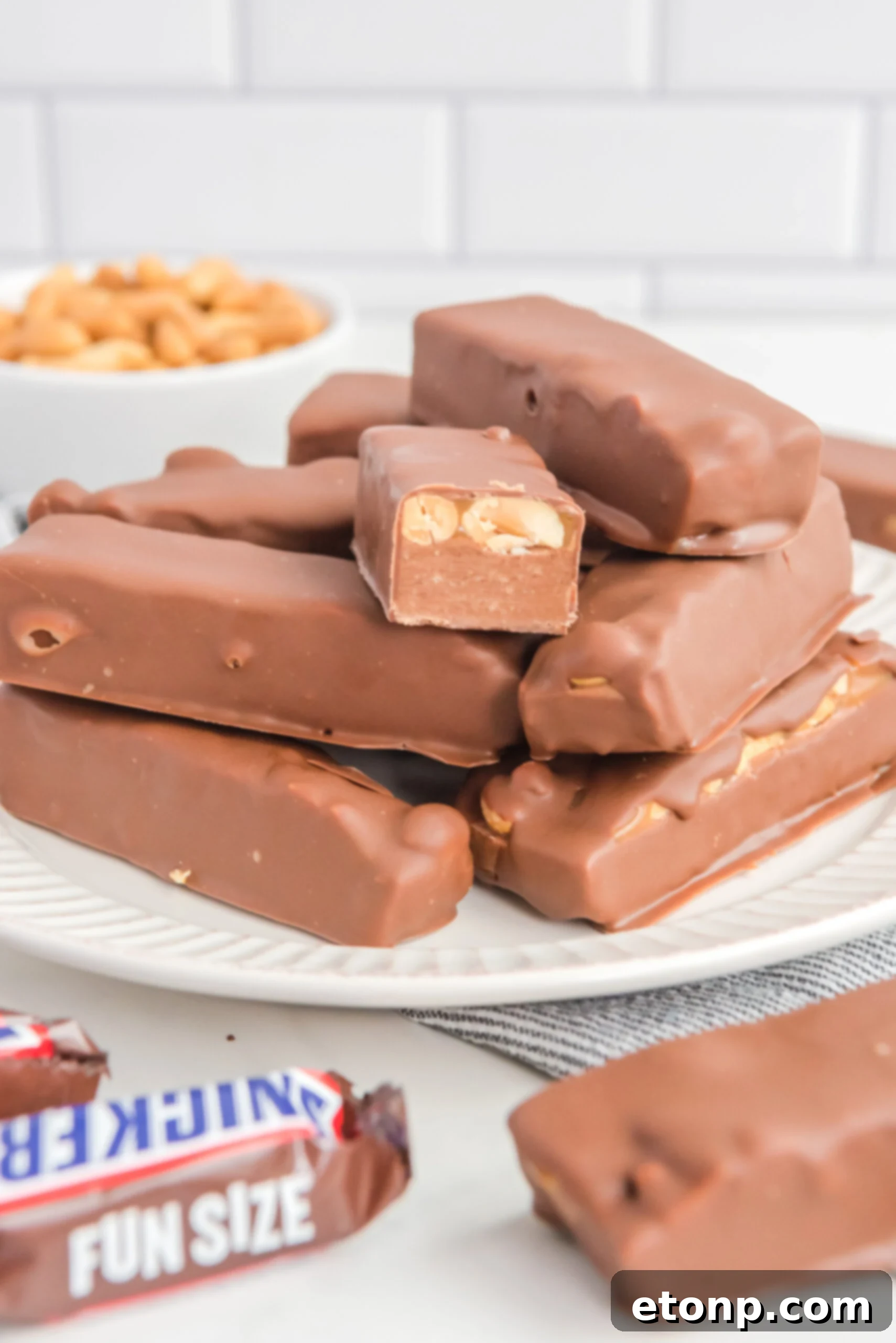 Front view of Homemade Snickers Bars stacked on a white plate with on bar cut in half.