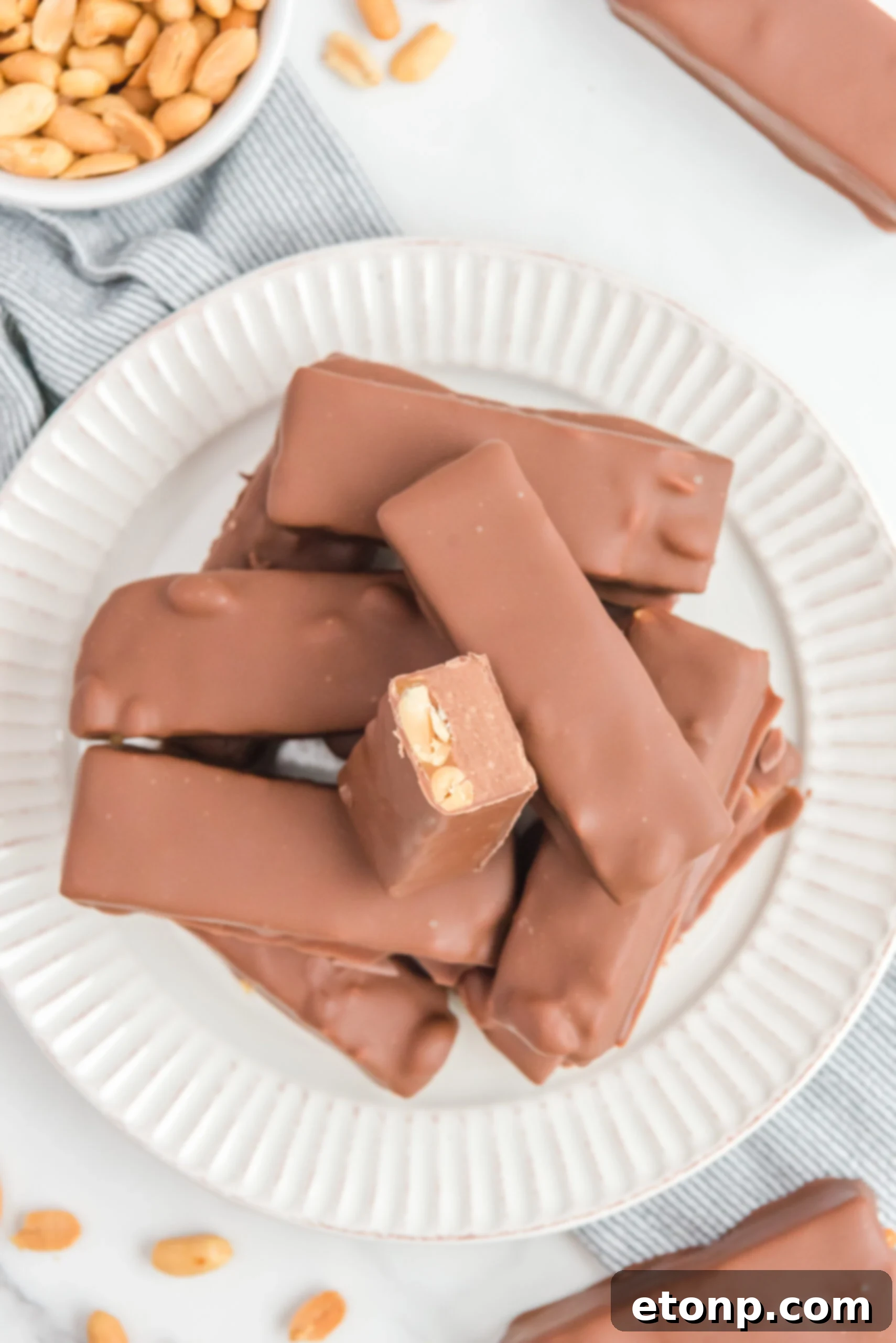 Overhead view of Homemade Snickers Bars stacked on a white plate with on bar cut in half.