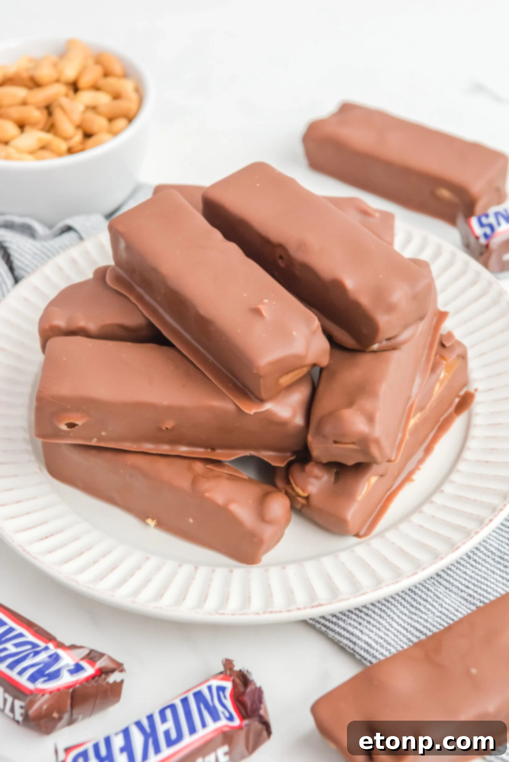 Homemade Snickers Candy Bars piled on a white serving plate 