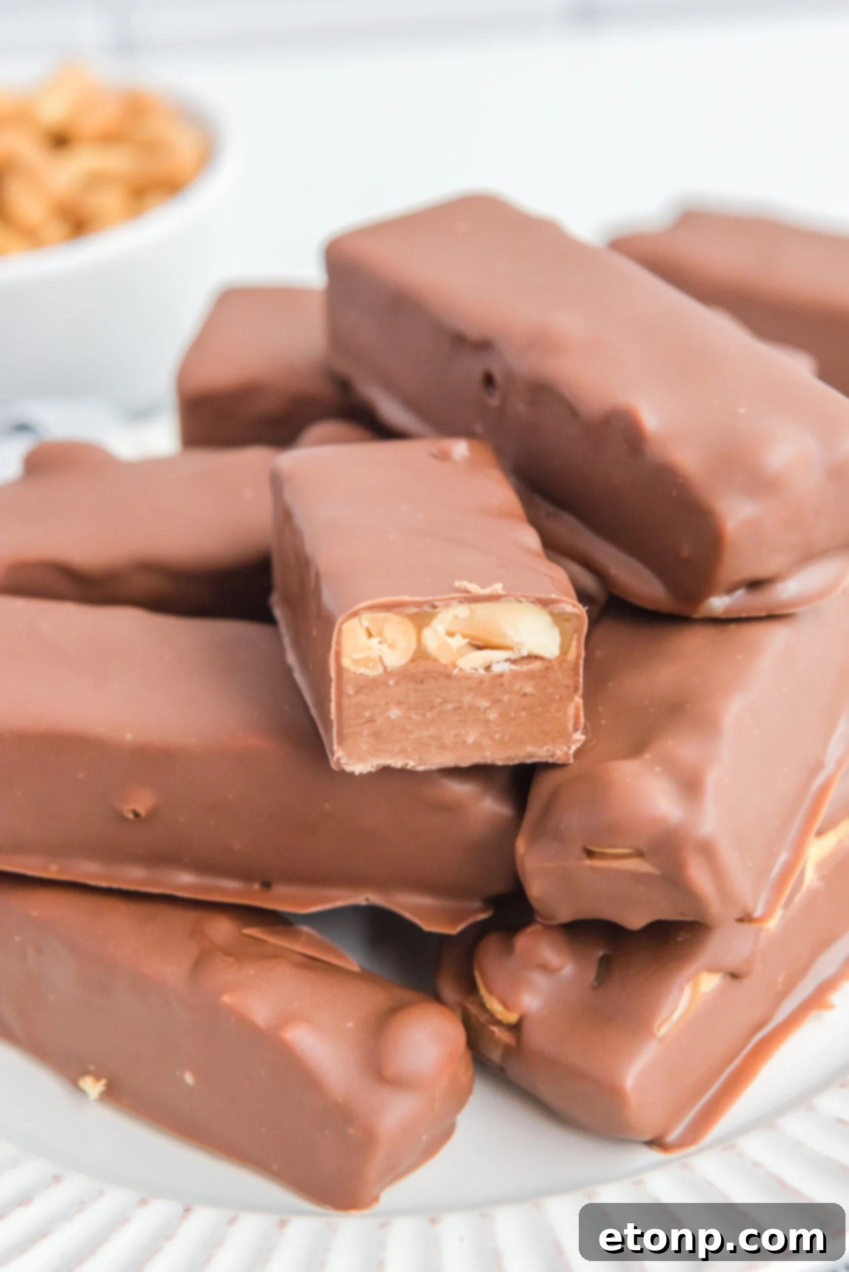 Homemade Snickers Candy Bars piled on a white serving plate with one cut open to show the inside