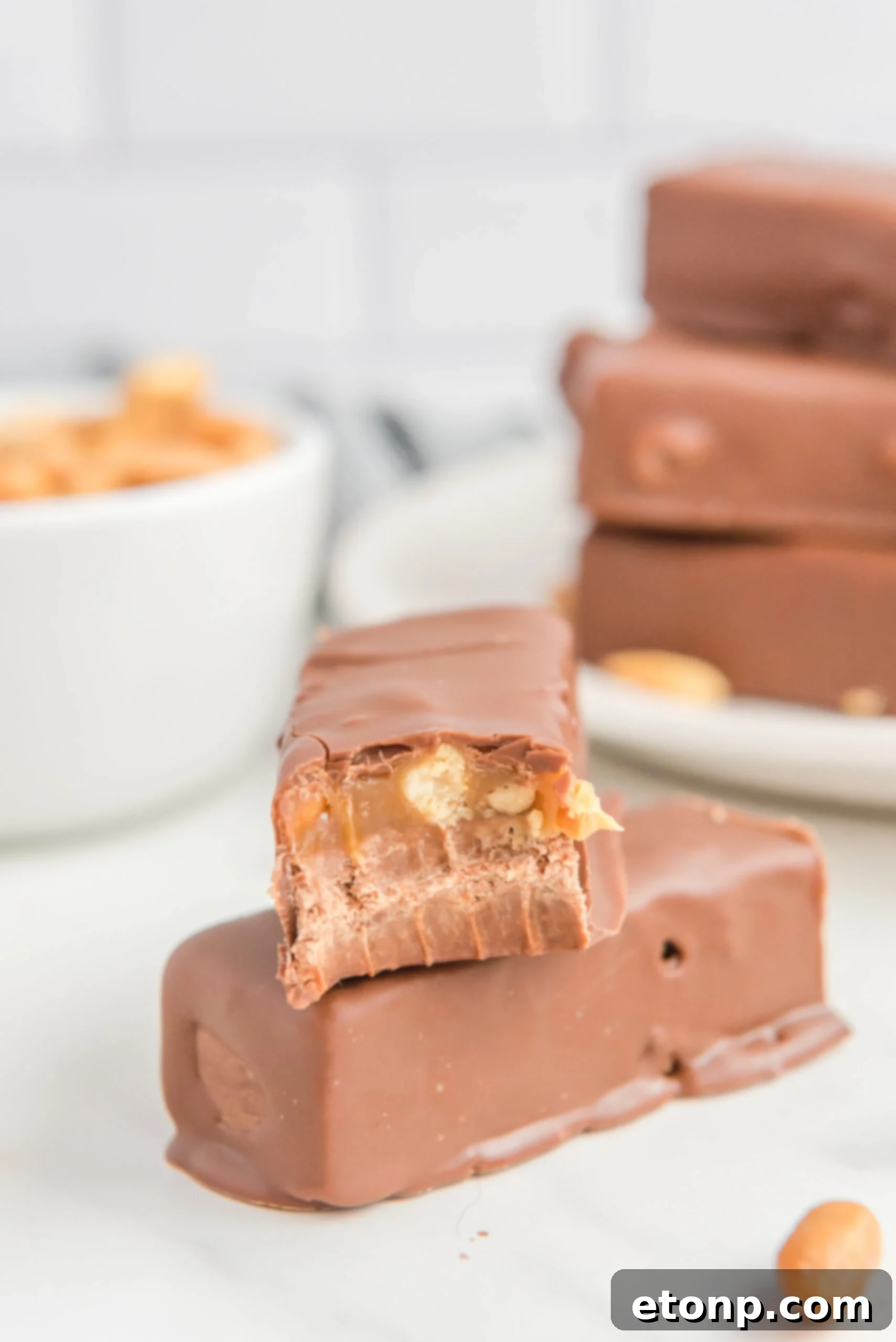 a couple Homemade Snickers Candy Bars on a table with a bite missing from one