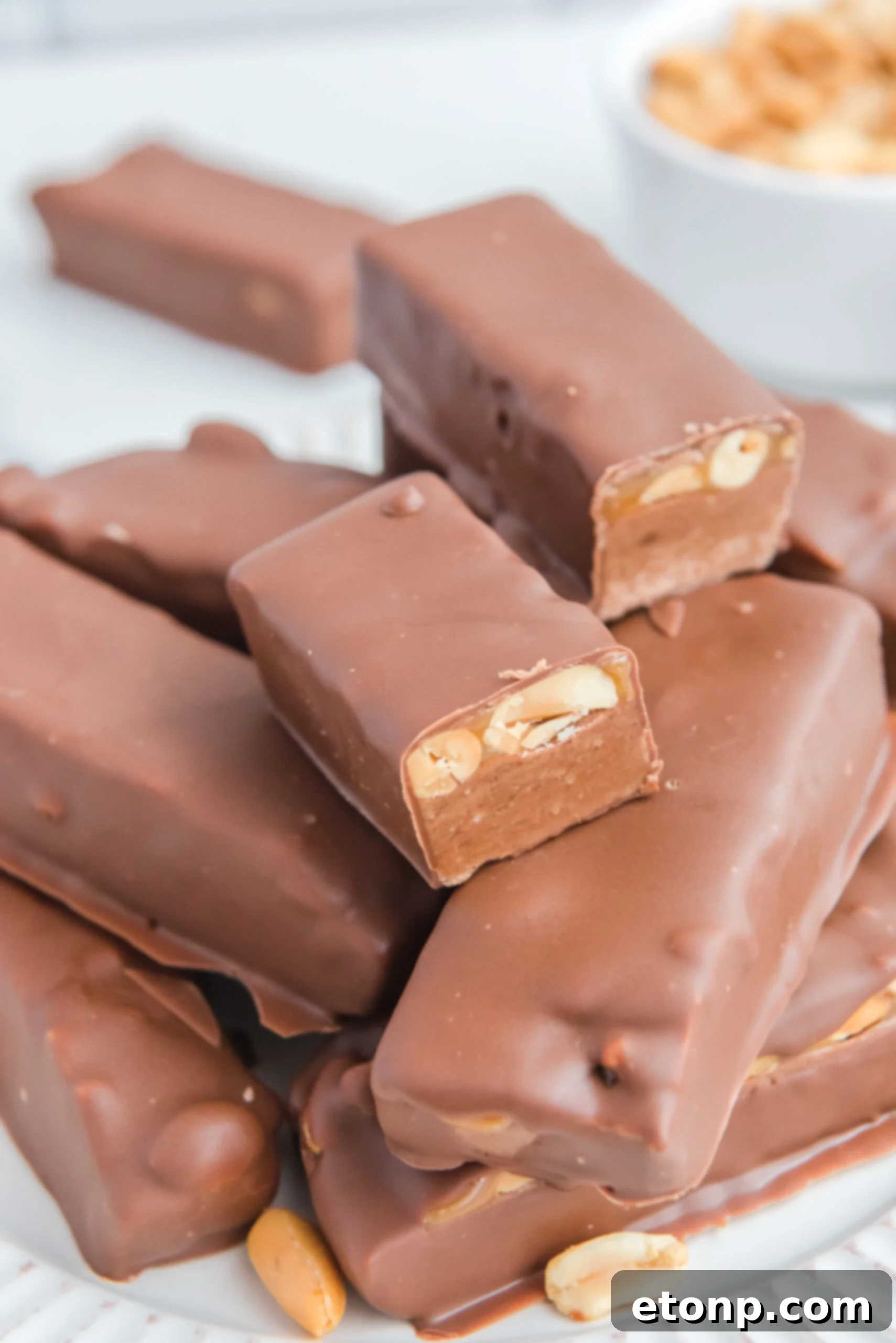 Homemade Snickers Candy Bars piled on a white serving plate with a bite missing from one