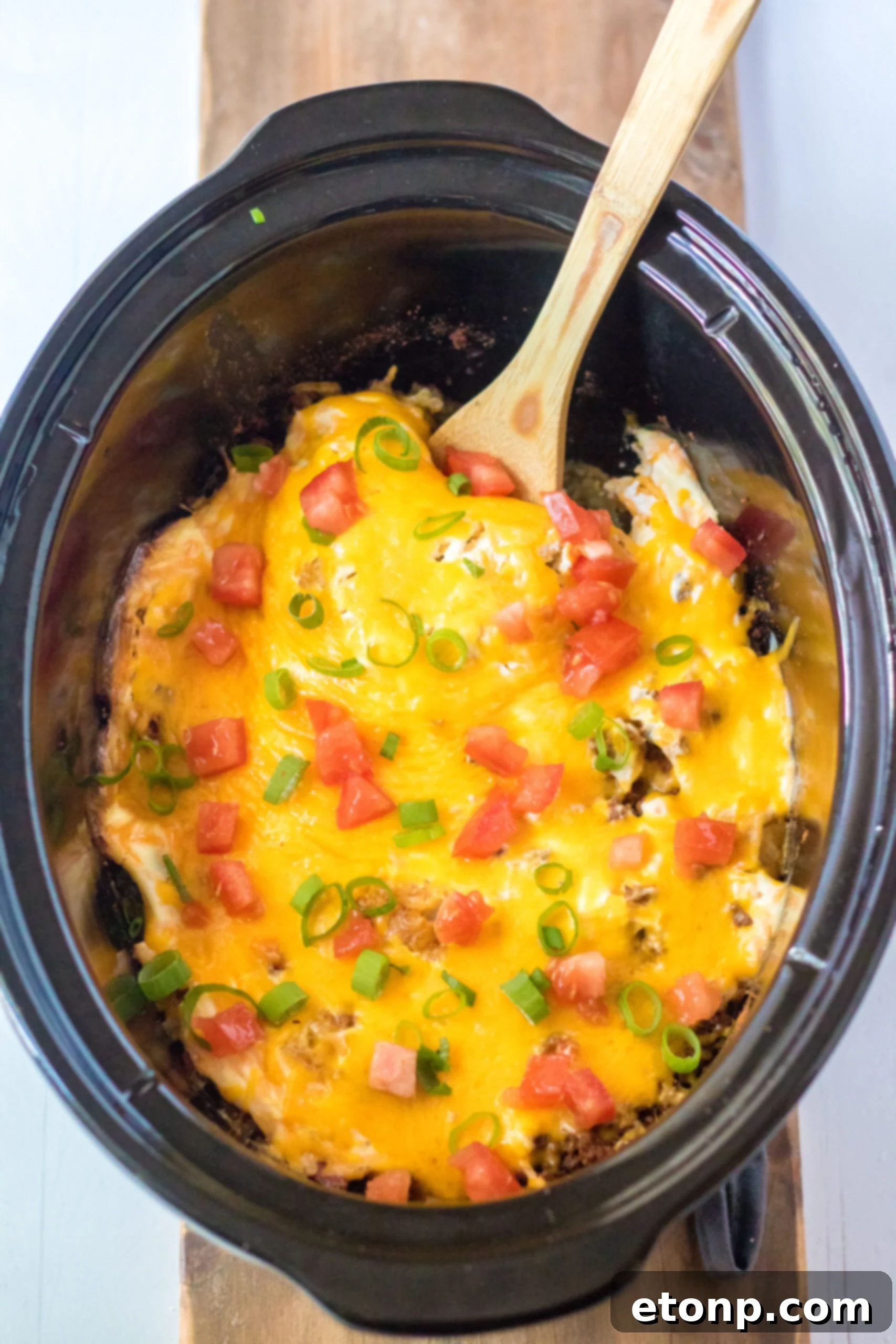 Overhead view of Slow Cooker John Wayne Casserole in a crock pot with a wooden spoon.