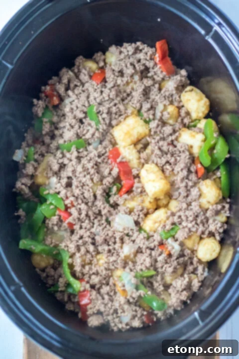 Ground beef and vegetables browning in a skillet for Slow Cooker John Wayne Casserole.