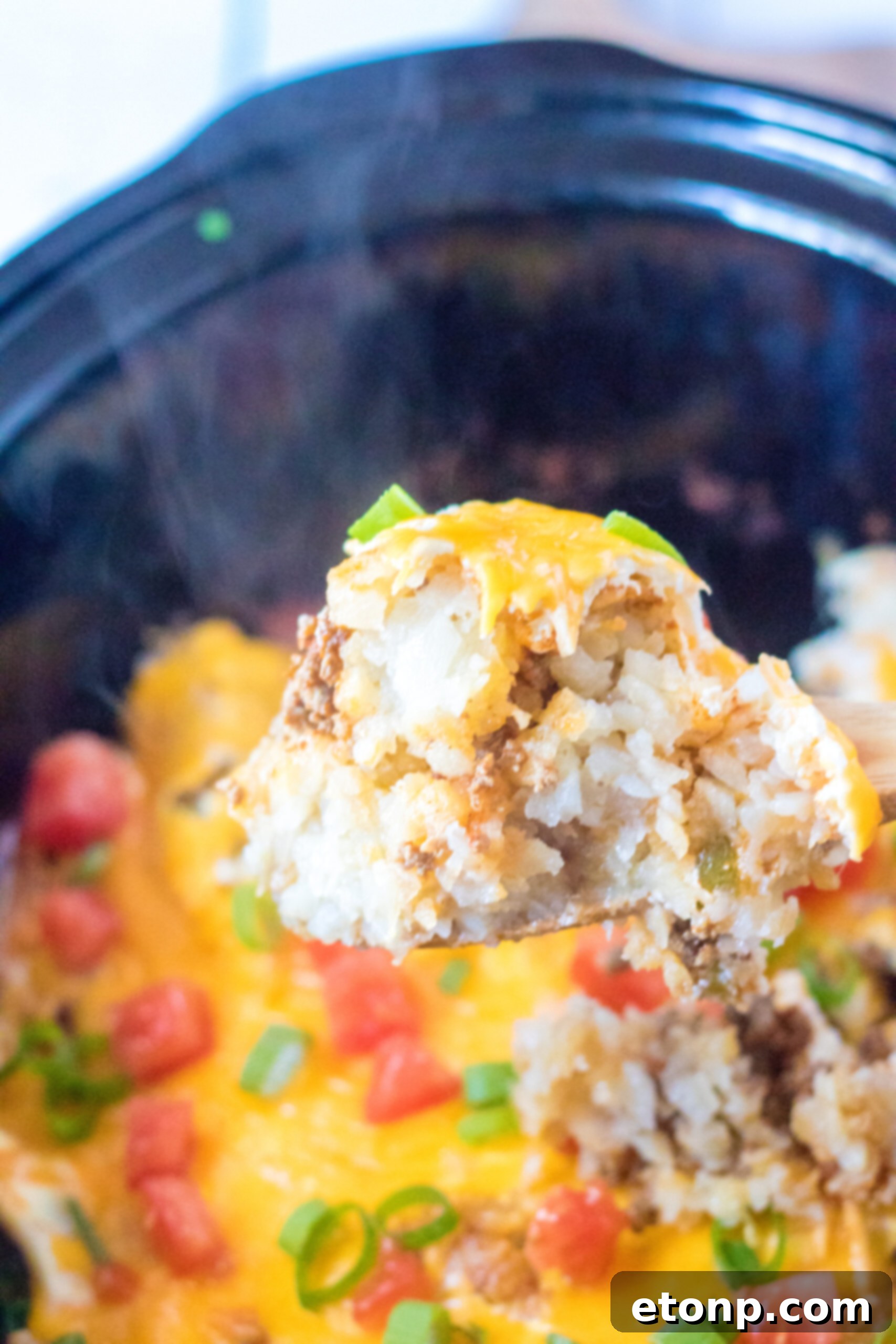 Close up view of a wooden spoon removing a serving of Slow Cooker John Wayne Casserole.