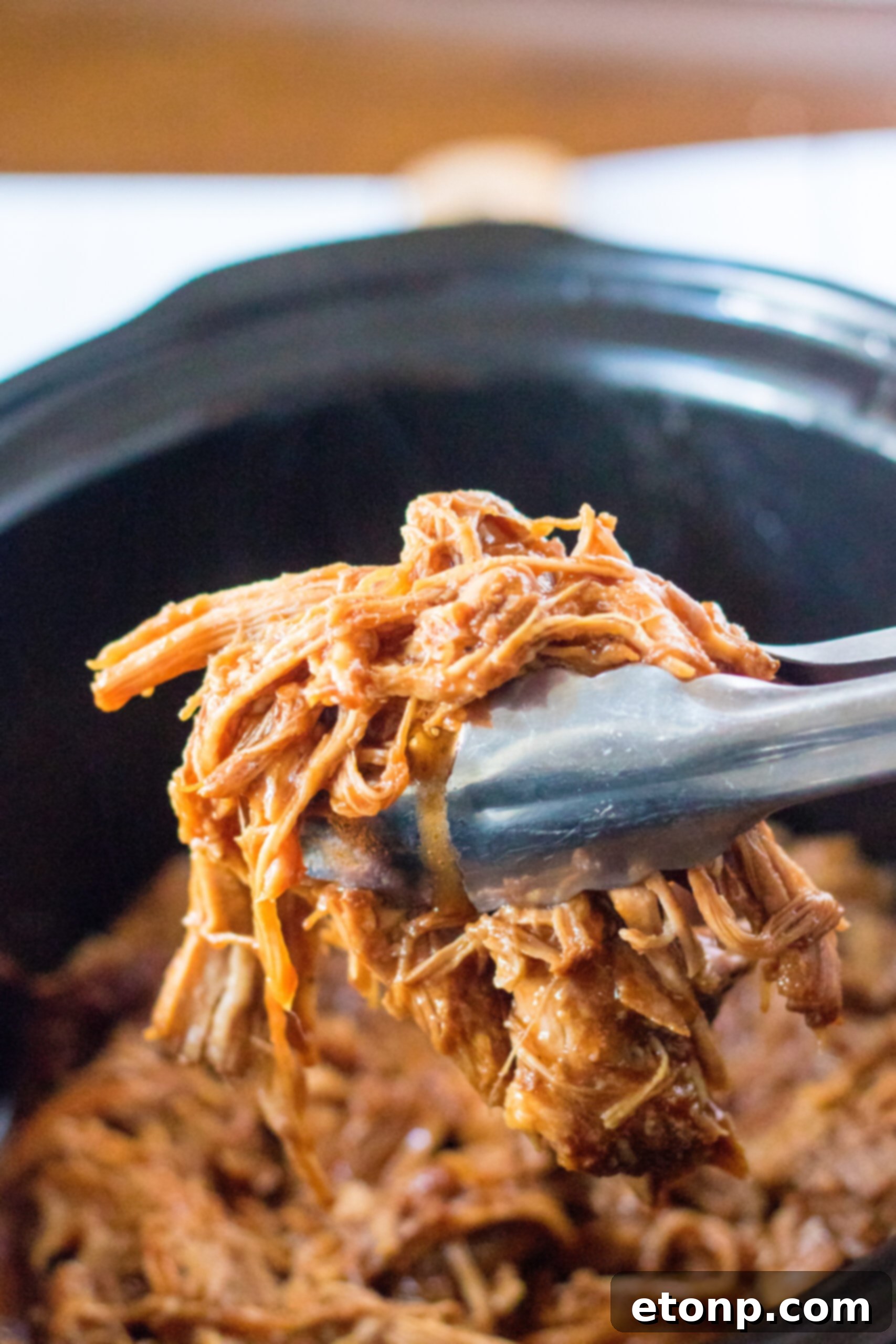 Front view of silver tongs holding a serving of Slow Cooker Cola Pulled Pork.
