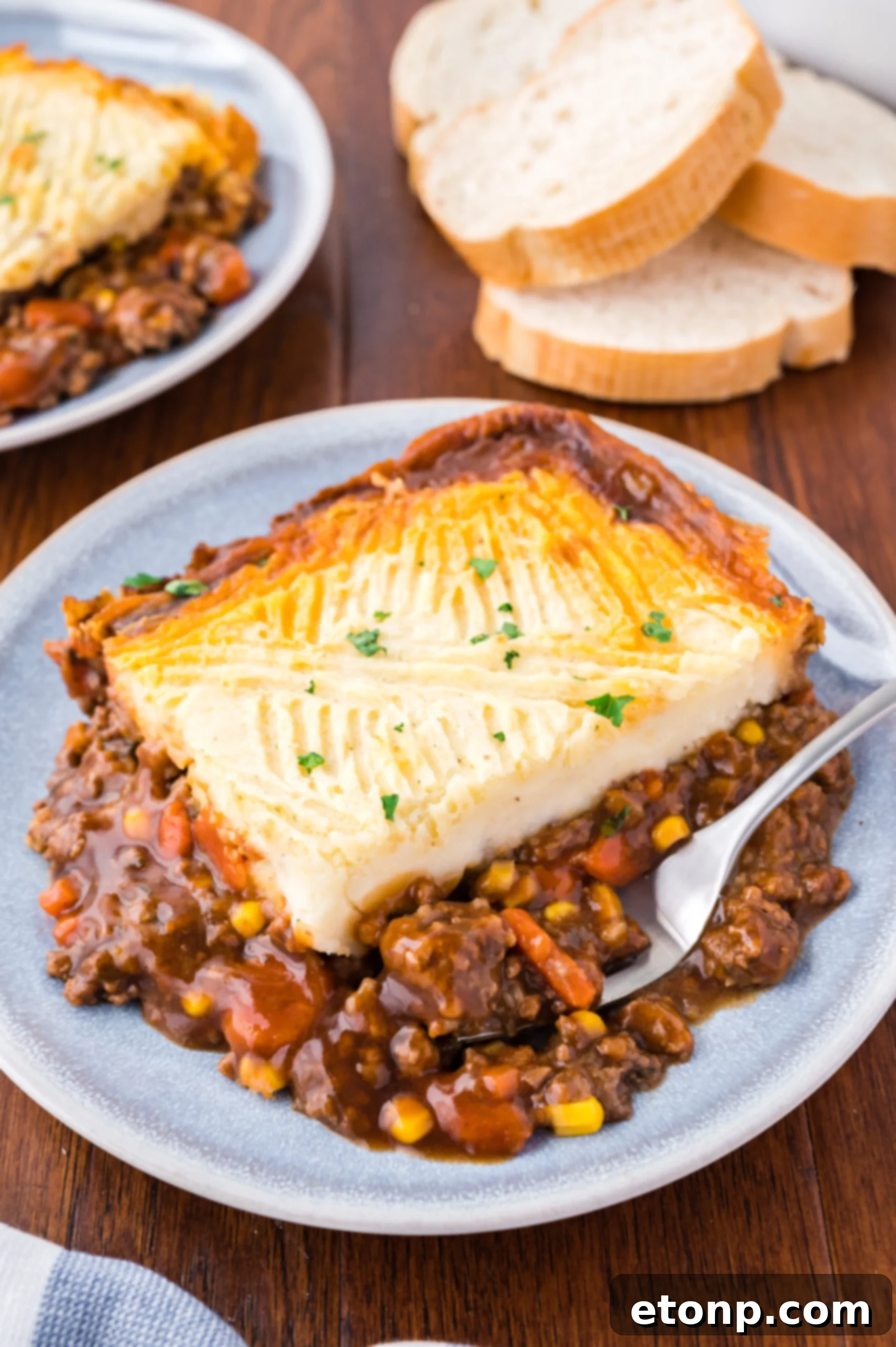Shepherd's pie on a gray and white plate with a silver fork on a wood table. 