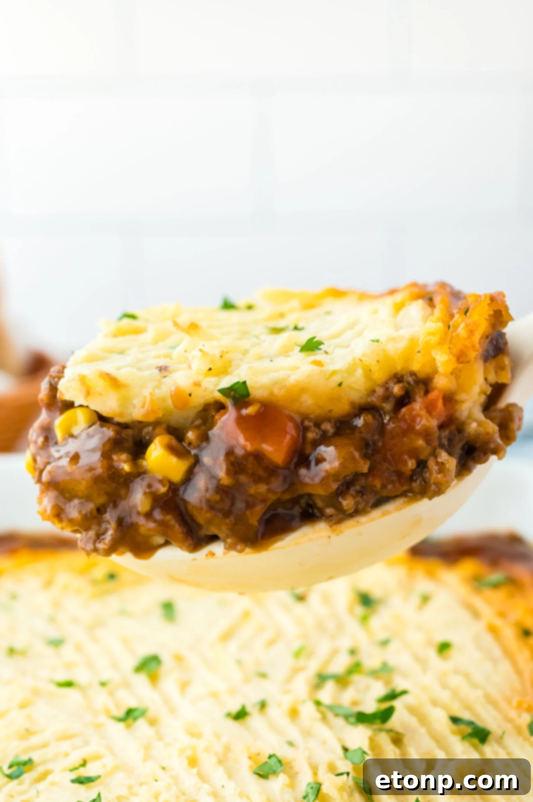 A large spoon removing Shepherd's Pie from the baking dish. 