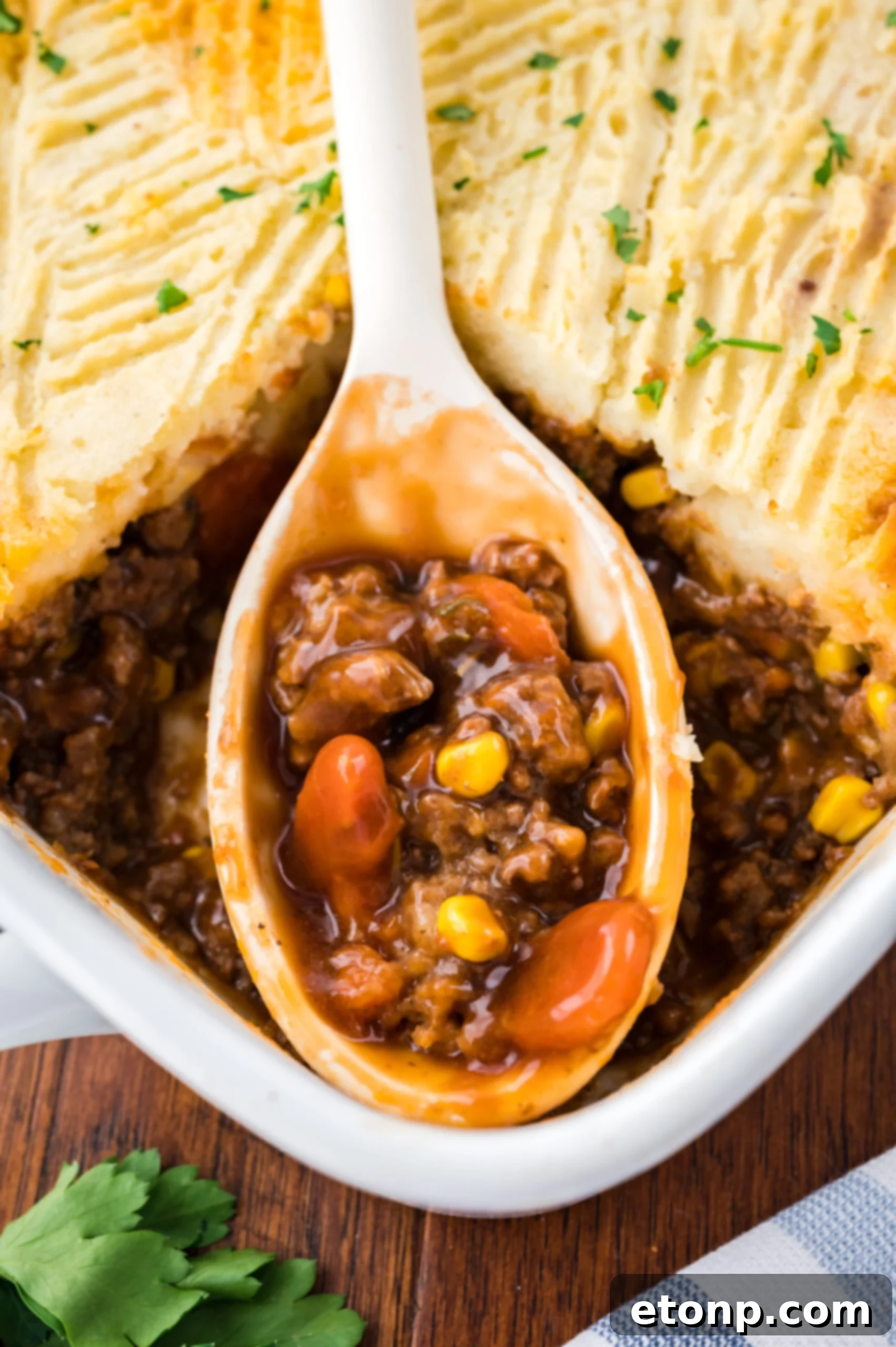 A large spoon removing Shepherd's Pie from the baking dish. 