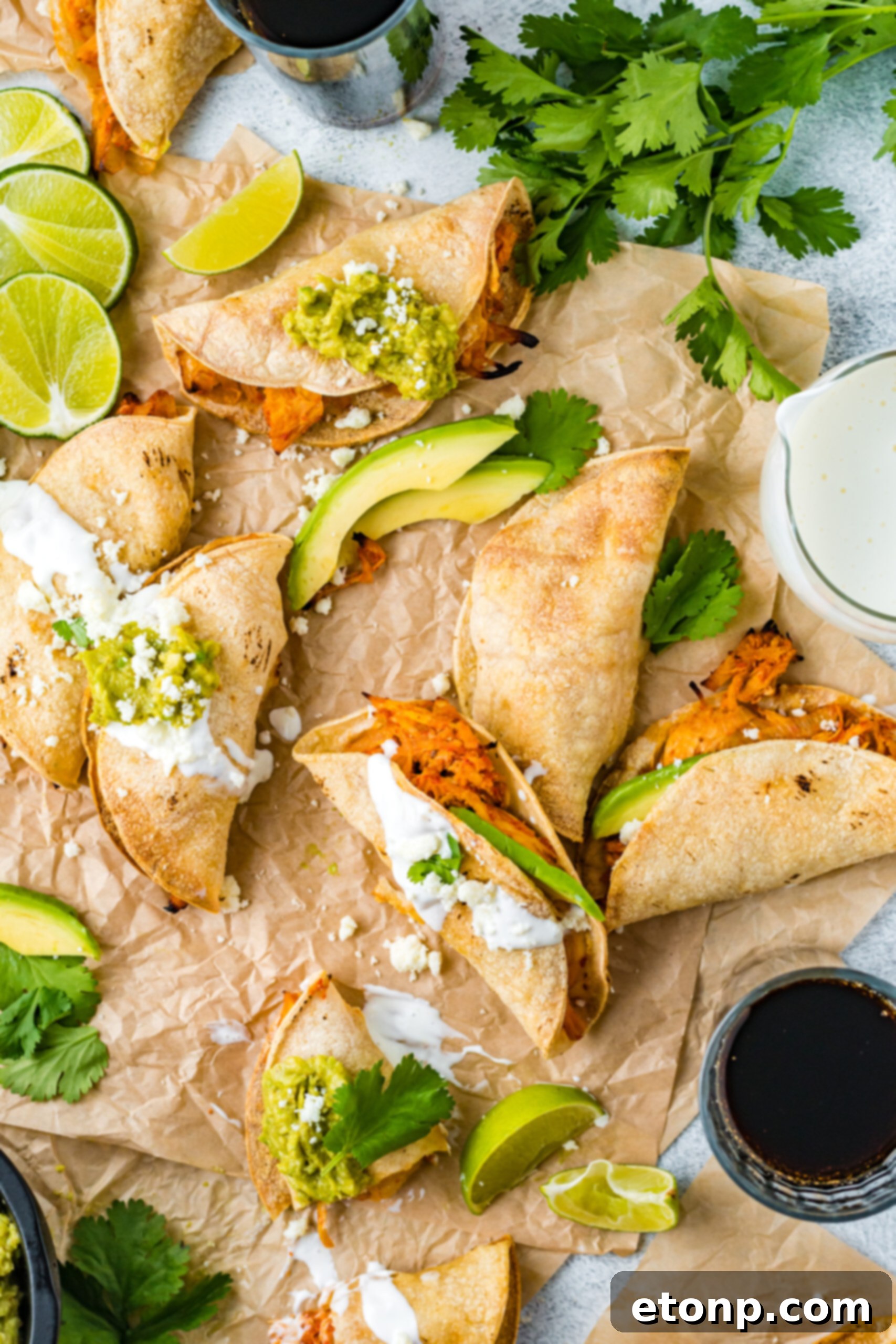 An inviting overhead view of a platter of Crispy Tinga Tacos, artfully arranged on parchment paper with fresh lime and avocado slices, creating a mouth-watering presentation.