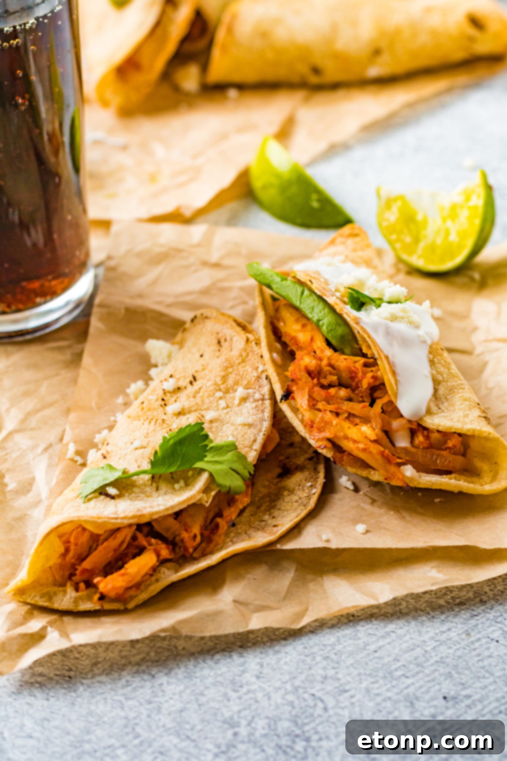Front view of two perfectly golden Crispy Tinga Tacos on a piece of parchment paper, highlighting their irresistible texture.
