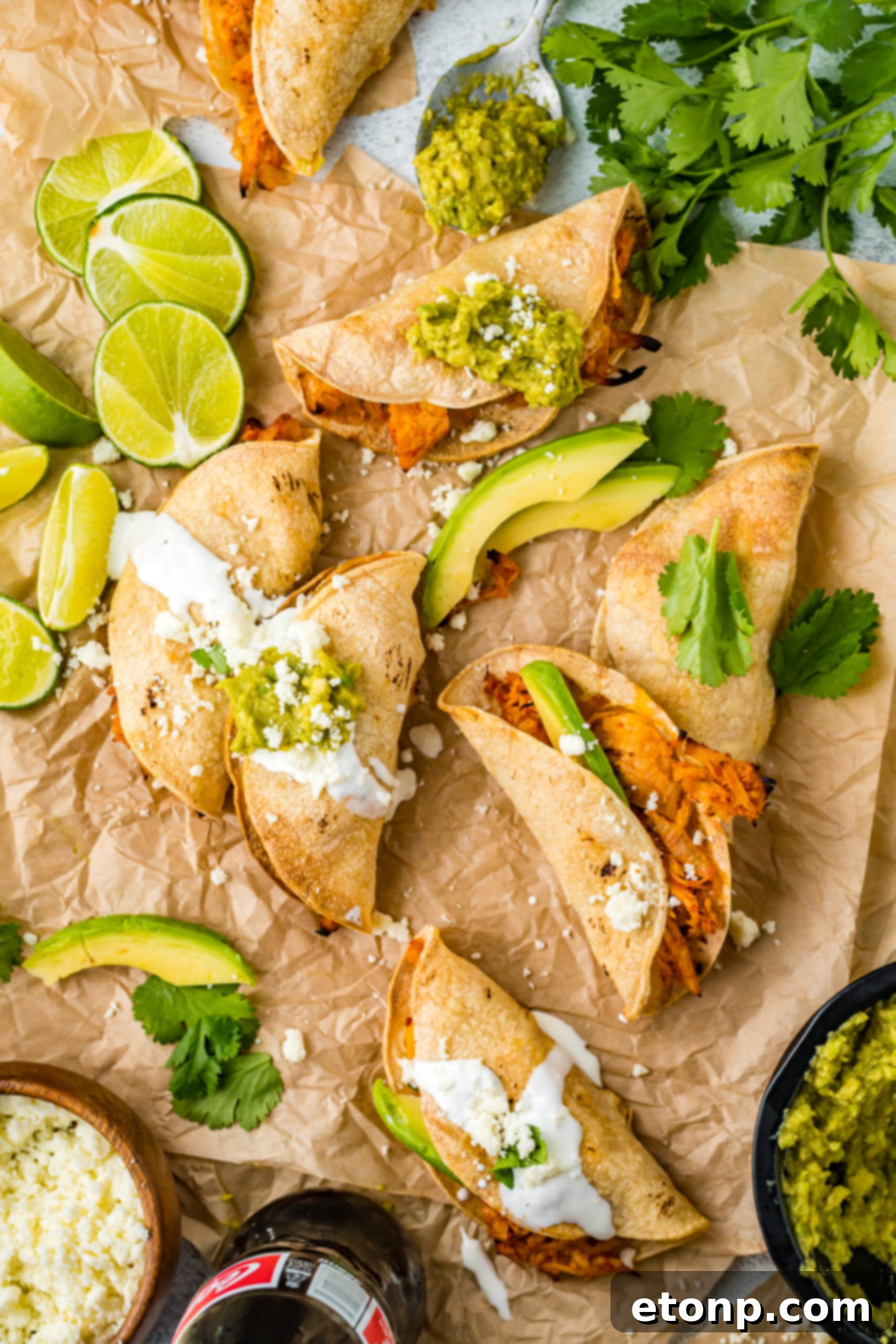 Another overhead perspective of Crispy Tinga Tacos on parchment, accompanied by fresh lime and avocado, highlighting the vibrant components of the dish.