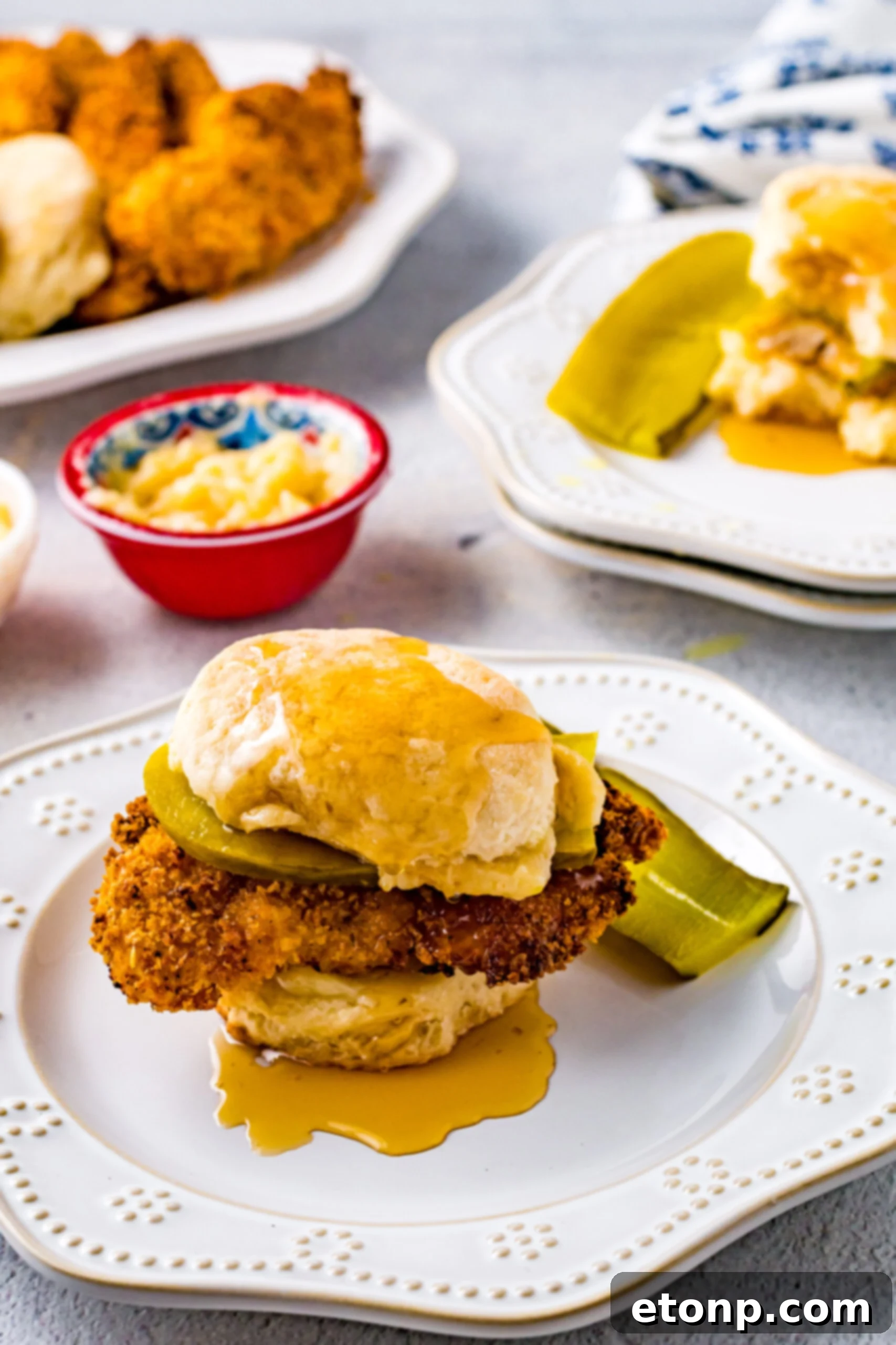 Front view of a Honey Butter Chicken Biscuit on a white plate with pickle slices, highlighting the generous honey butter application and crispy chicken.