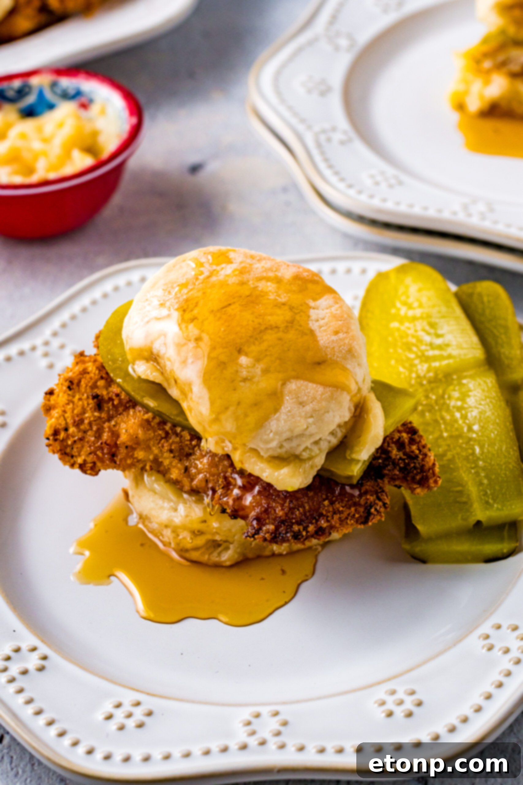 Honey Butter Chicken Biscuit served on a white plate with two crisp pickle slices on the side, adding a tangy contrast.