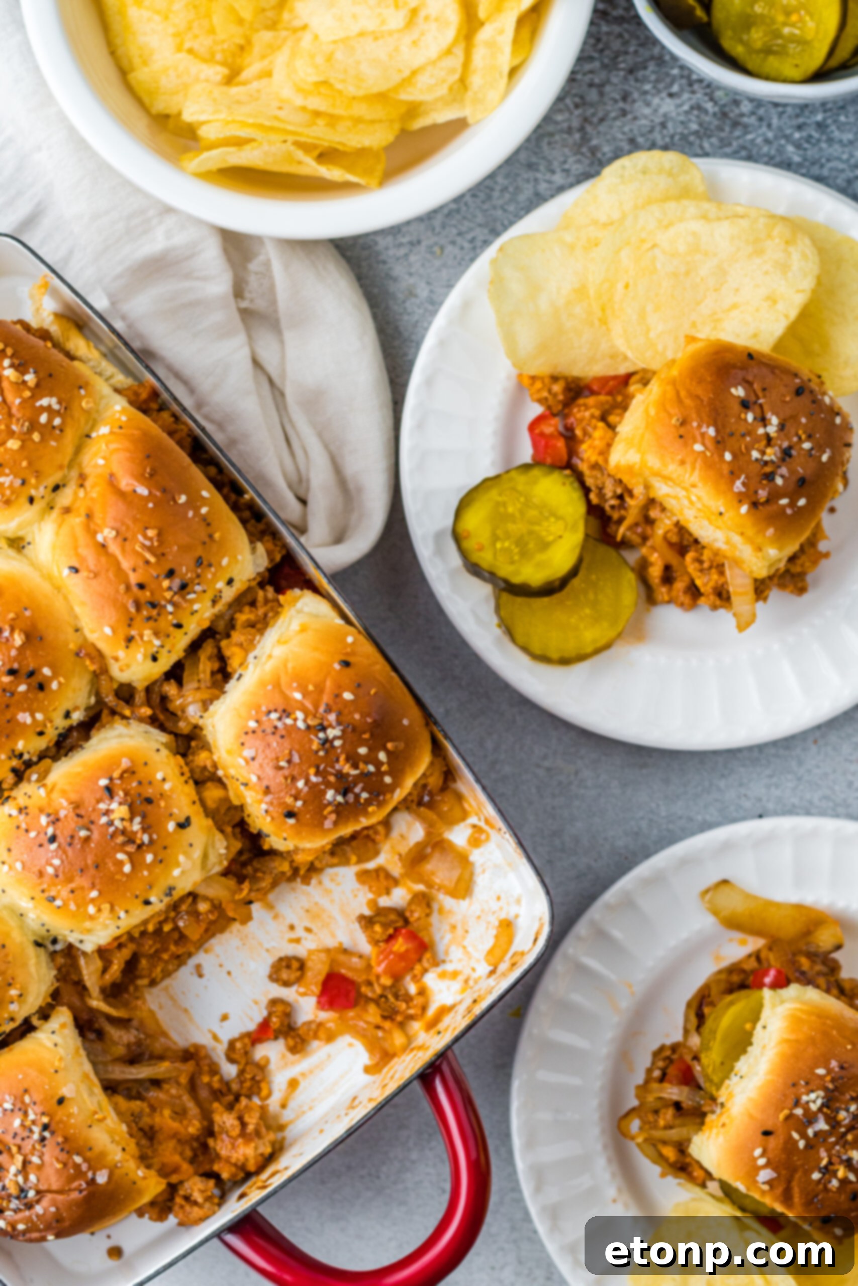 Overhead view of Cheesy Chicken Sloppy Joe Sliders on white plates served with pickle slices and chips.