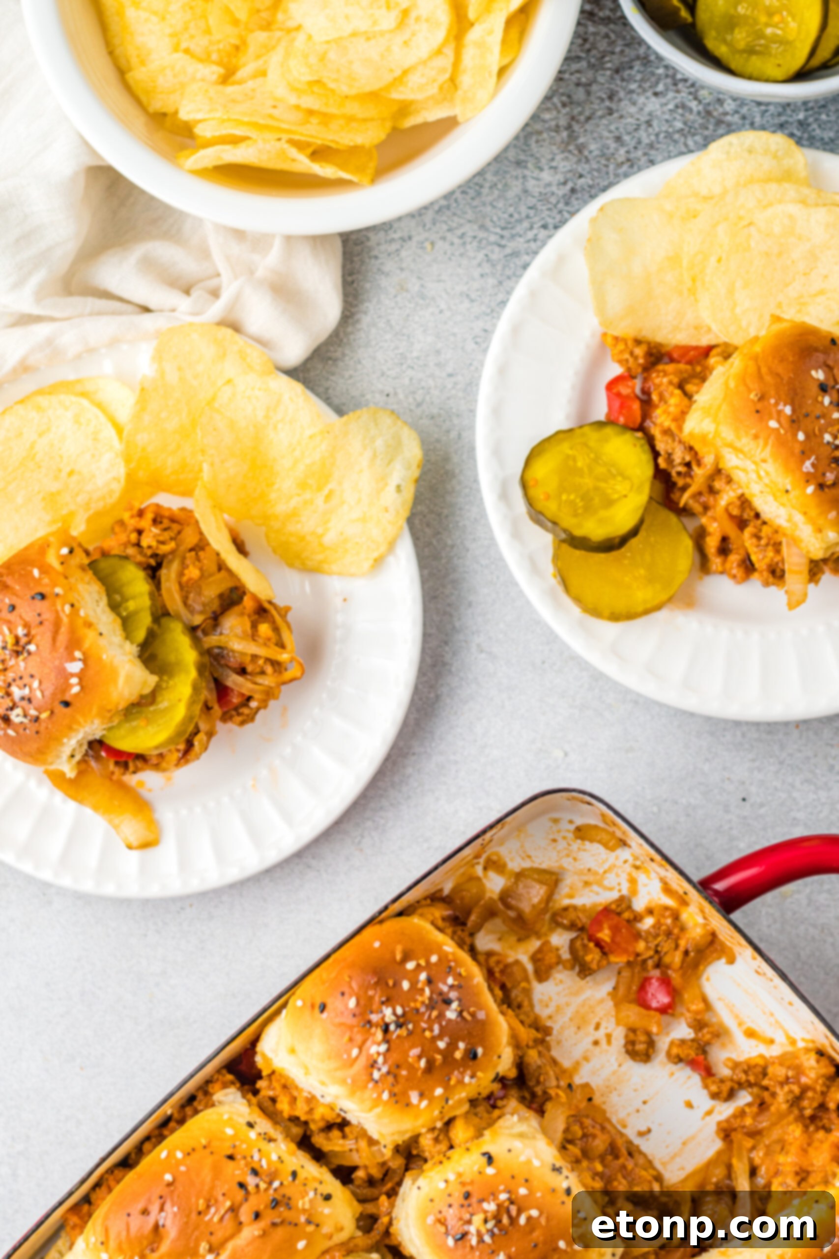 Overhead view of Cheesy Chicken Sloppy Joe Sliders on white plates served with pickle slices and chips.