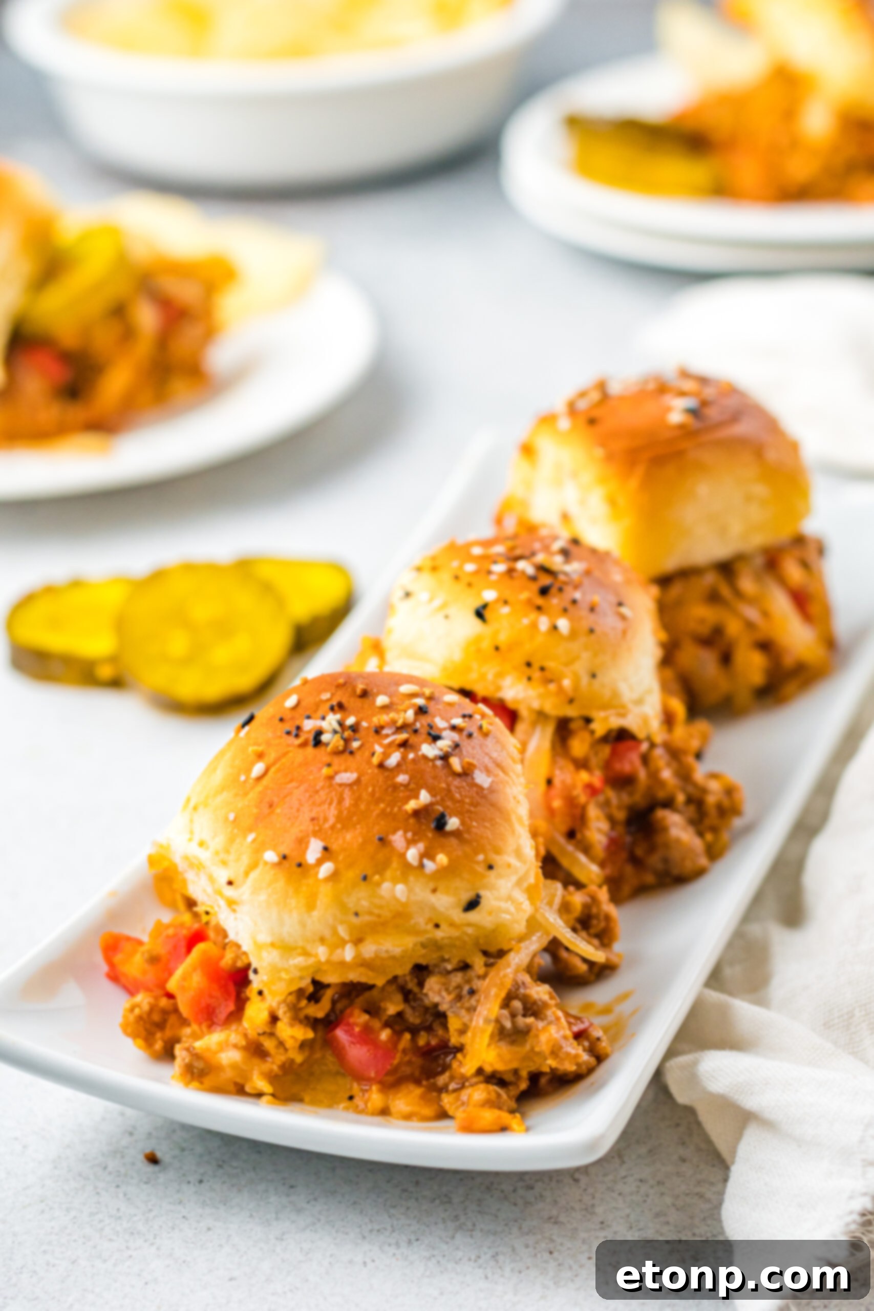 Front view of three Cheesy Chicken Sloppy Joe Sliders on a white serving dish.