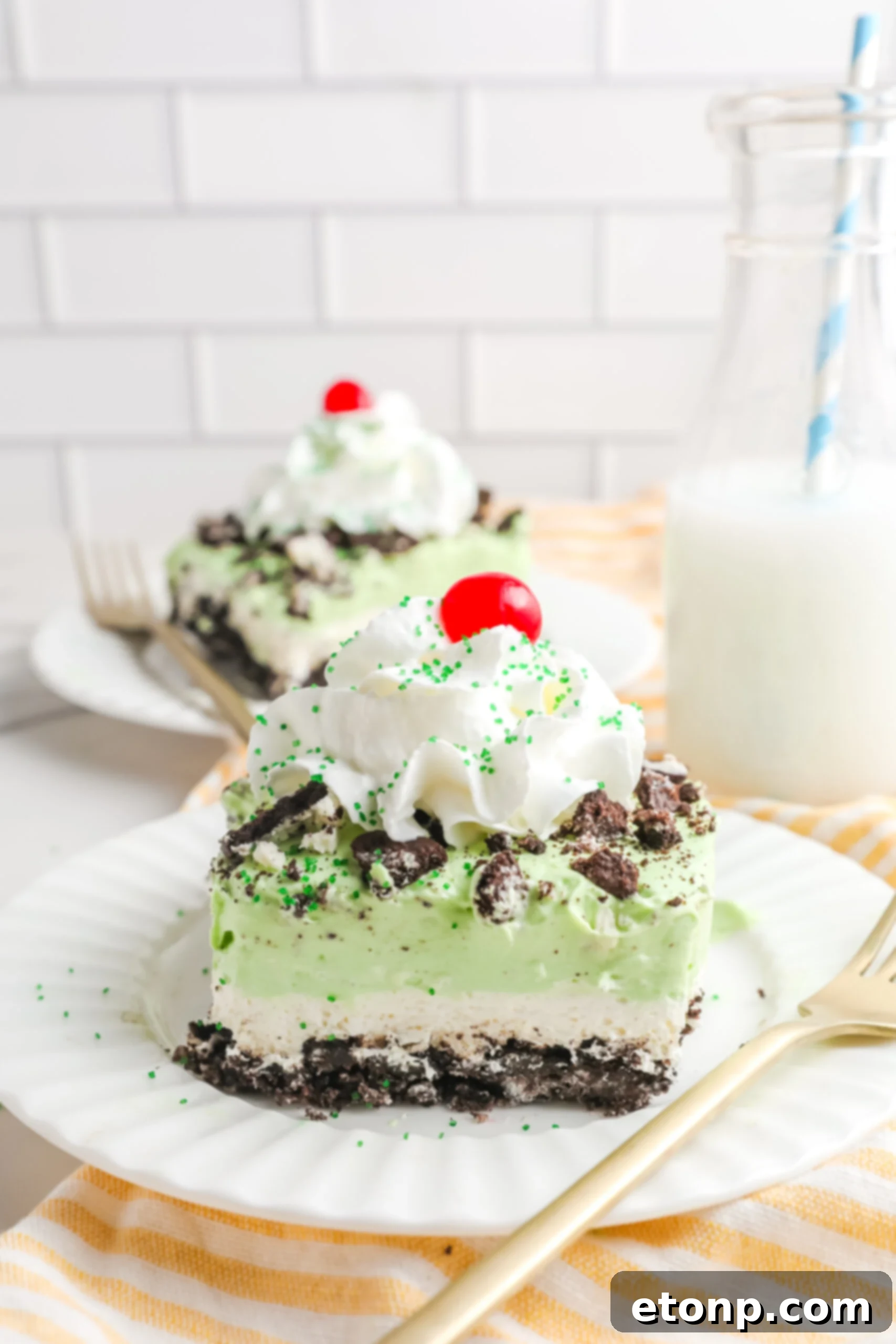 Two generous pieces of Shamrock Lasagna on pristine white plates, accompanied by elegant gold forks, ready to be enjoyed.