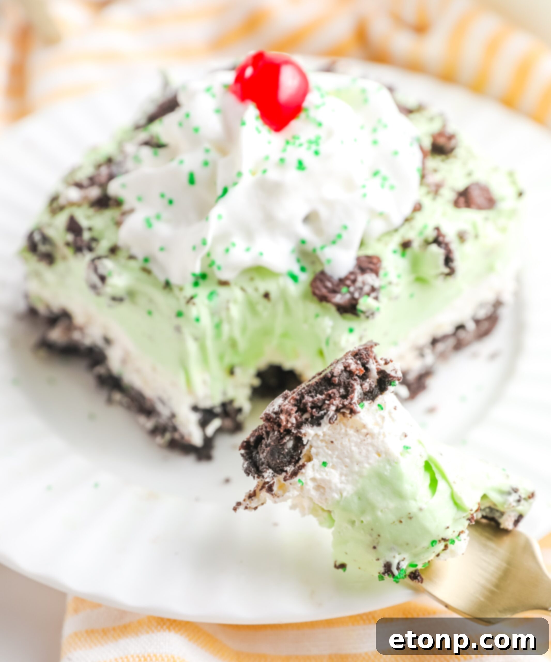 A beautiful side angle of the Shamrock Lasagna, elegantly topped with a generous dollop of whipped cream and a bright red maraschino cherry, ready for serving.