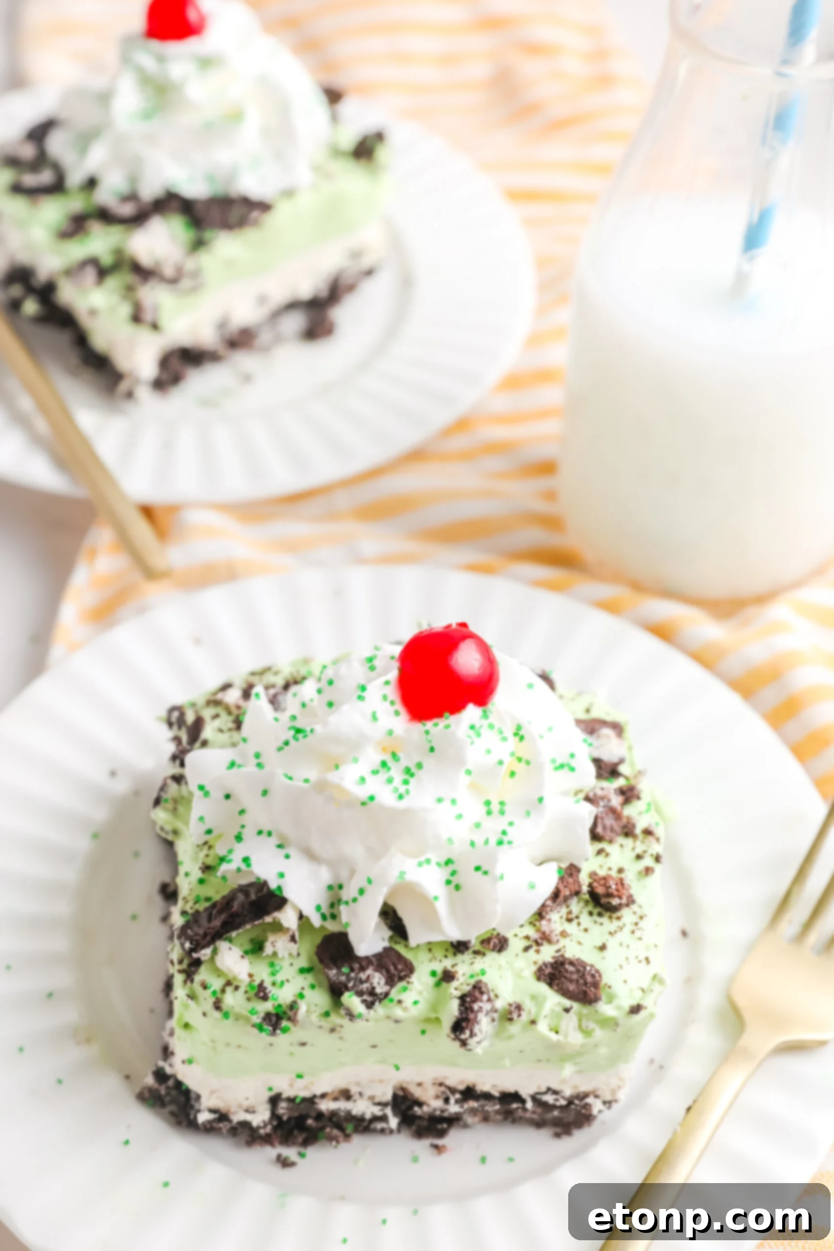 Two perfectly portioned pieces of Shamrock Lasagna dessert, presented on elegant white plates with accompanying gold forks, inviting indulgence.