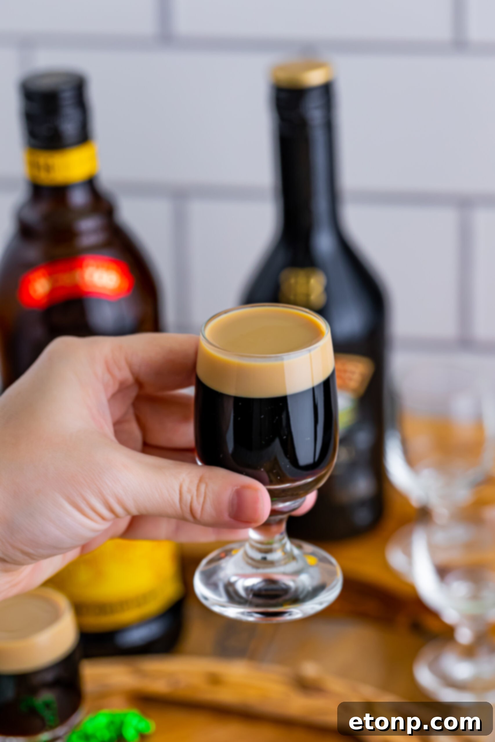 A hand holding a perfectly layered Baby Guinness Shot, ready to be enjoyed, against a softly blurred background.