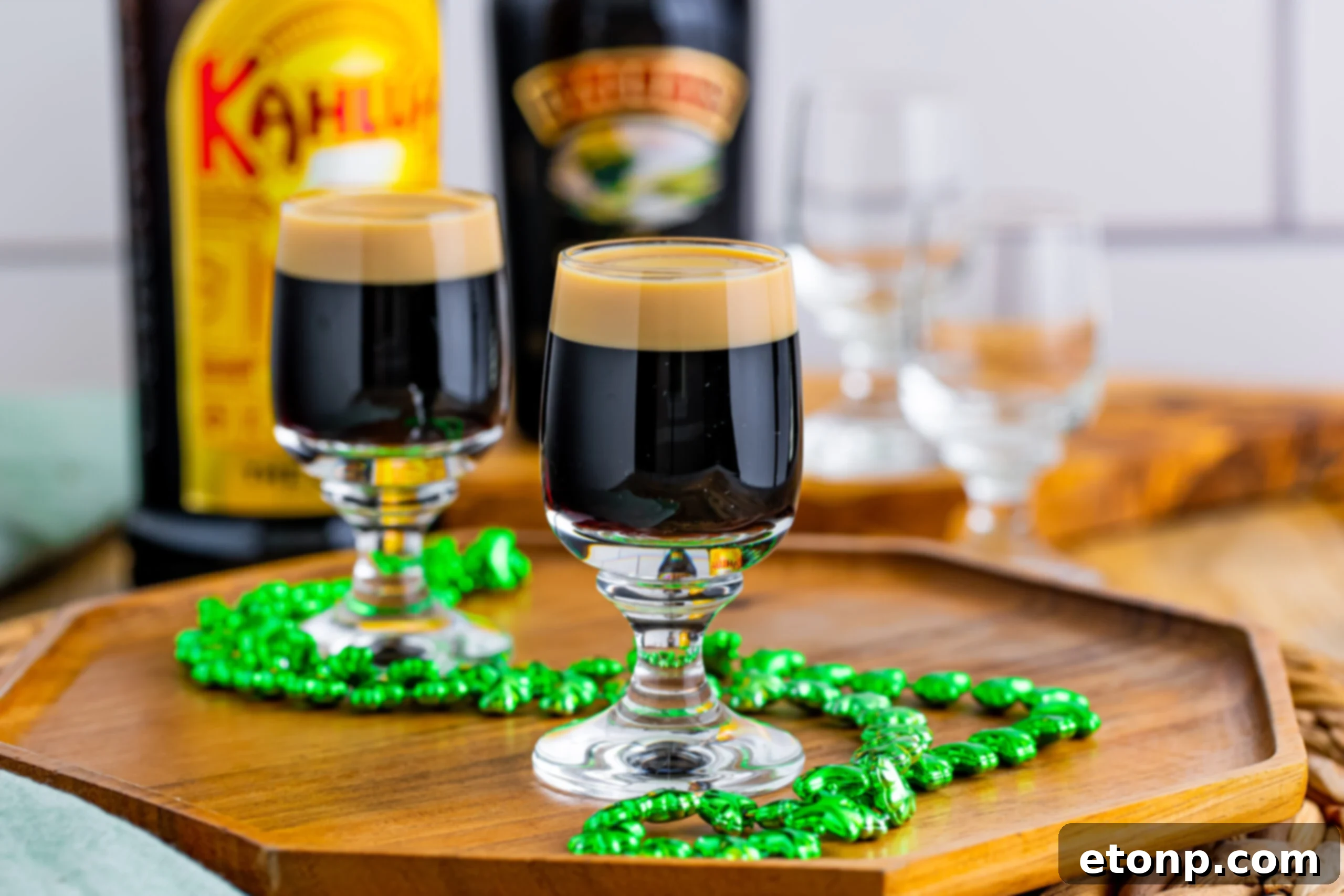 Two enticing Baby Guinness Shots on a wooden board, accompanied by a decorative green shamrock necklace, showcasing their appeal for themed celebrations or casual enjoyment.