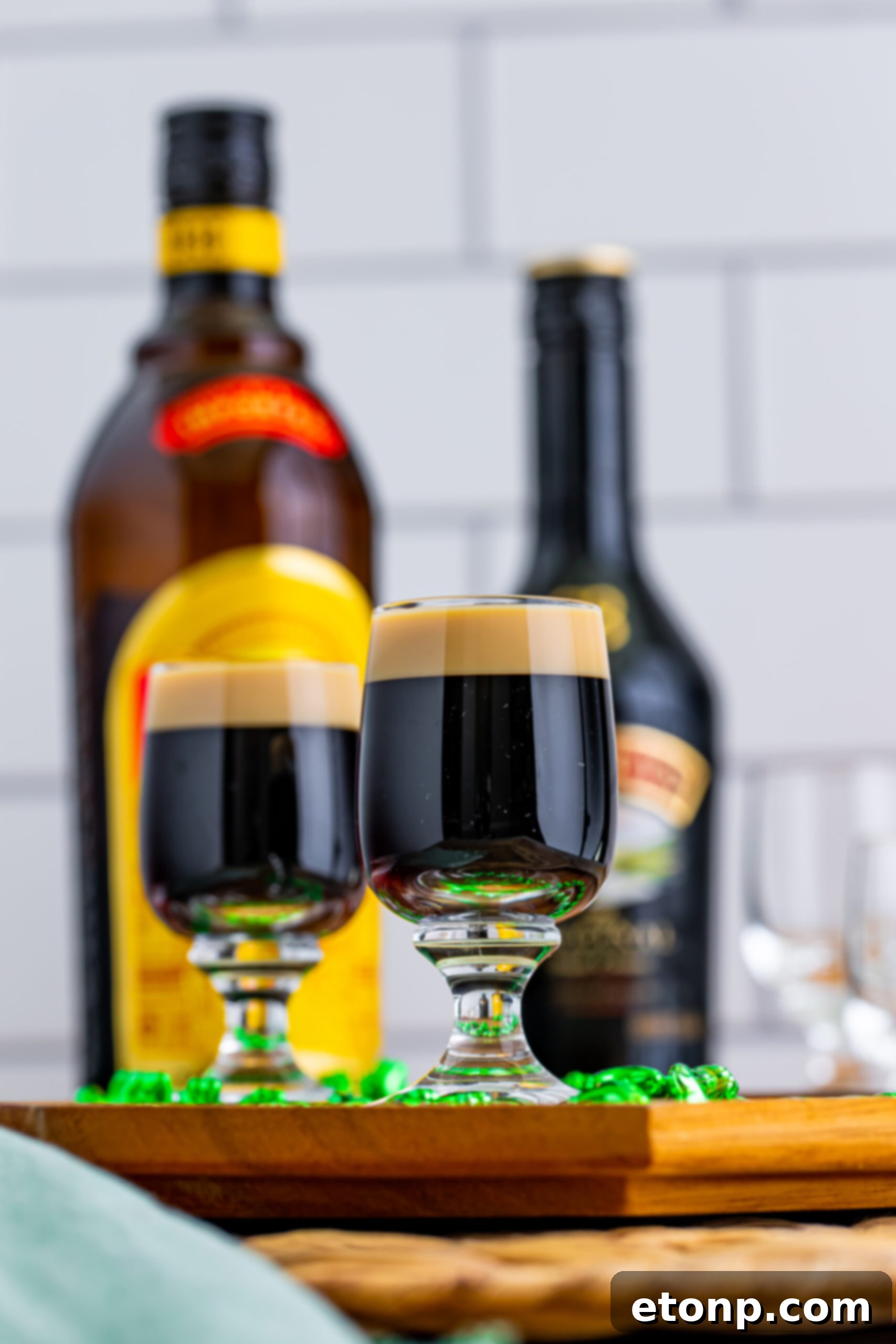 A final, enticing image of two Baby Guinness Shots, perfectly crafted and presented on a wooden board, accompanied by a green shamrock necklace, inviting drinkers to savor their unique flavor.