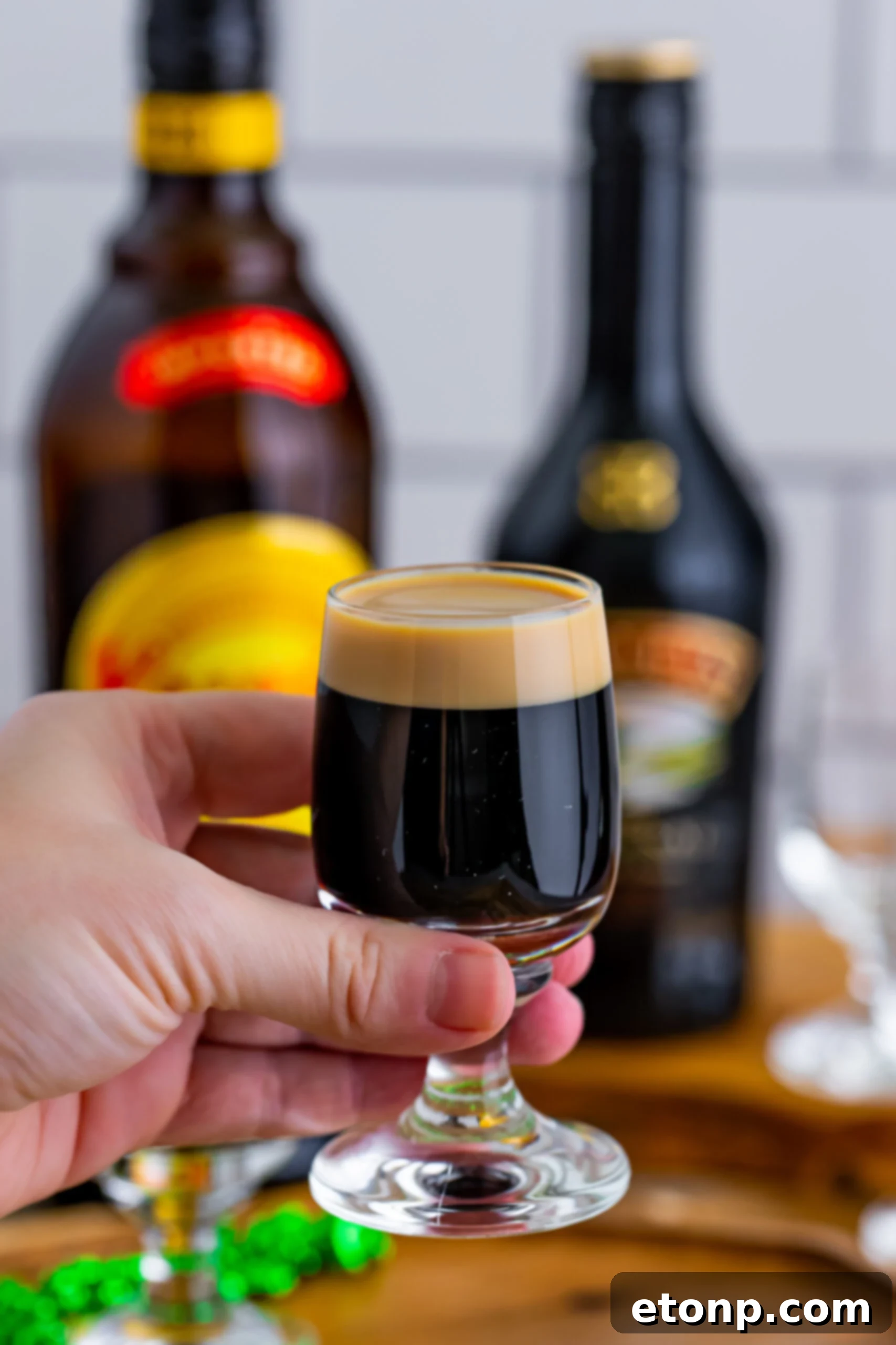A hand holds a perfectly prepared Baby Guinness Shot, highlighting the distinct layers of coffee liqueur and Irish cream.