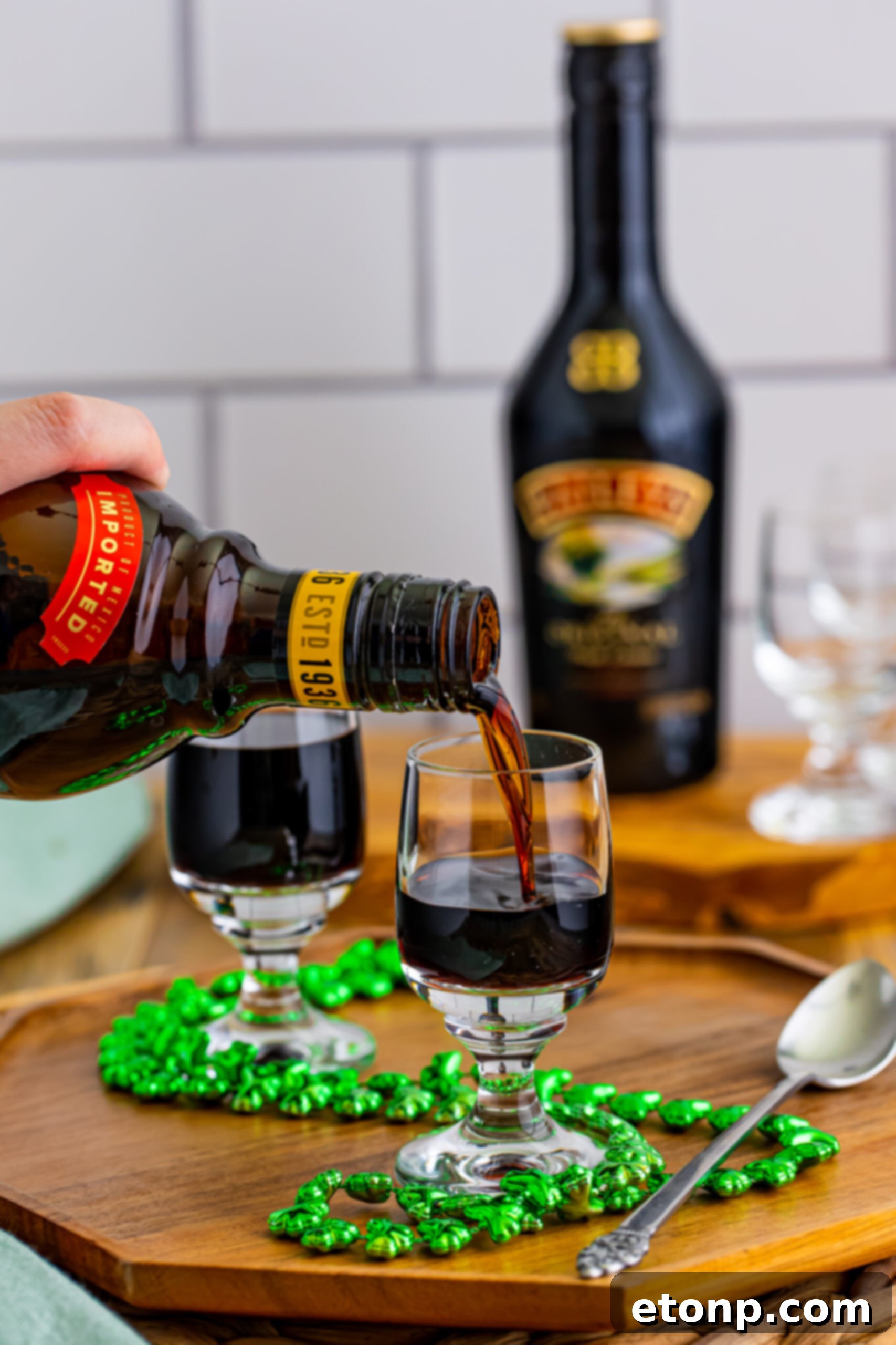 A close-up of a shot glass being filled three-quarters full with dark, chilled Kahlua, forming the base of a Baby Guinness Shot.