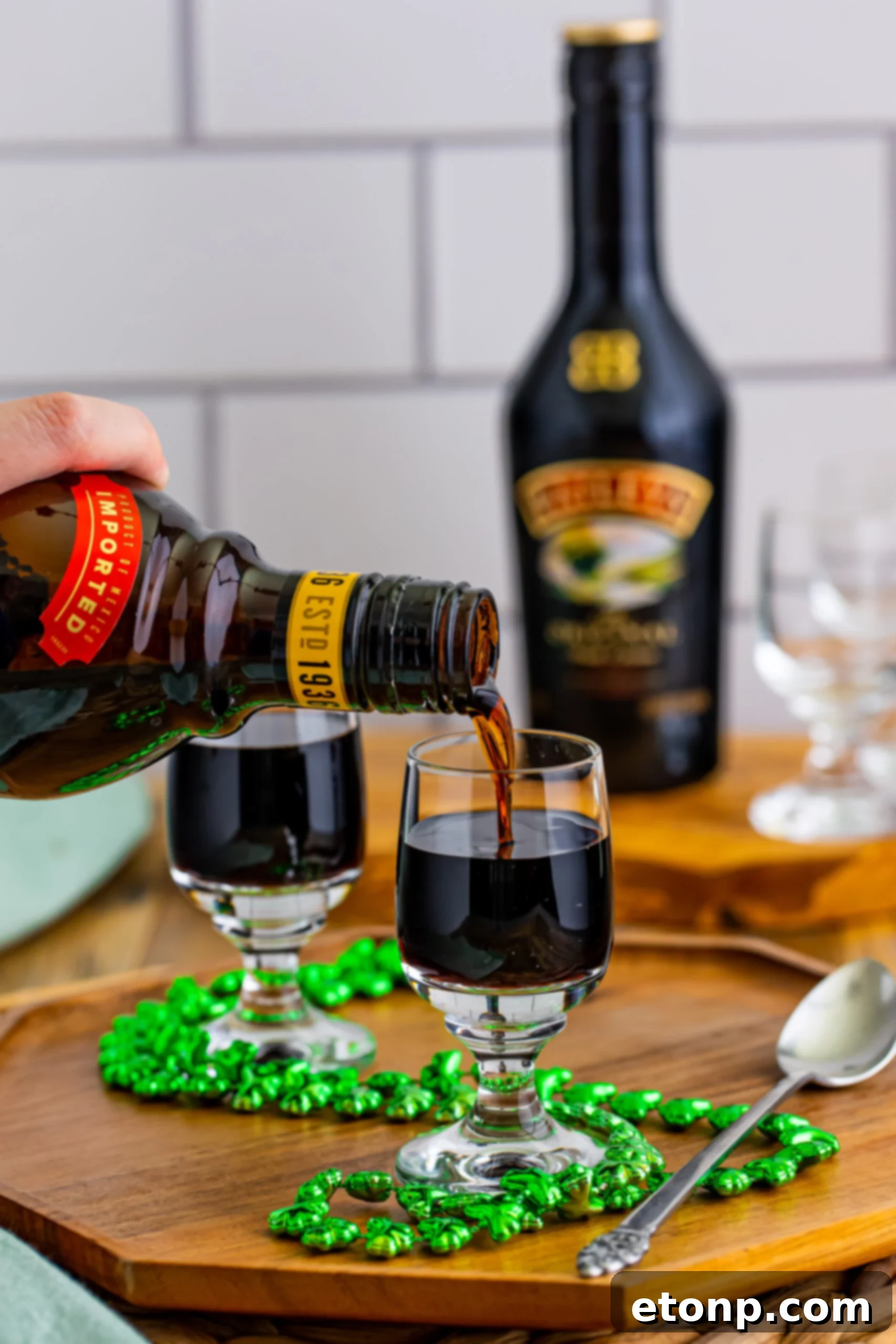 The critical step of inverting a slender spoon over the Kahlua, illustrating the technique for careful layering of the Bailey's Irish Cream.