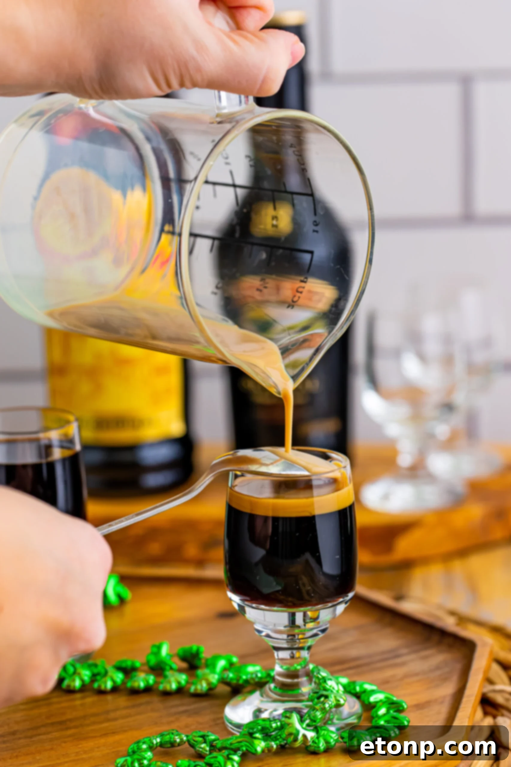A stream of creamy Bailey's Irish Cream being gently poured over the back of a spoon, creating a distinct white layer atop the Kahlua in a shot glass.