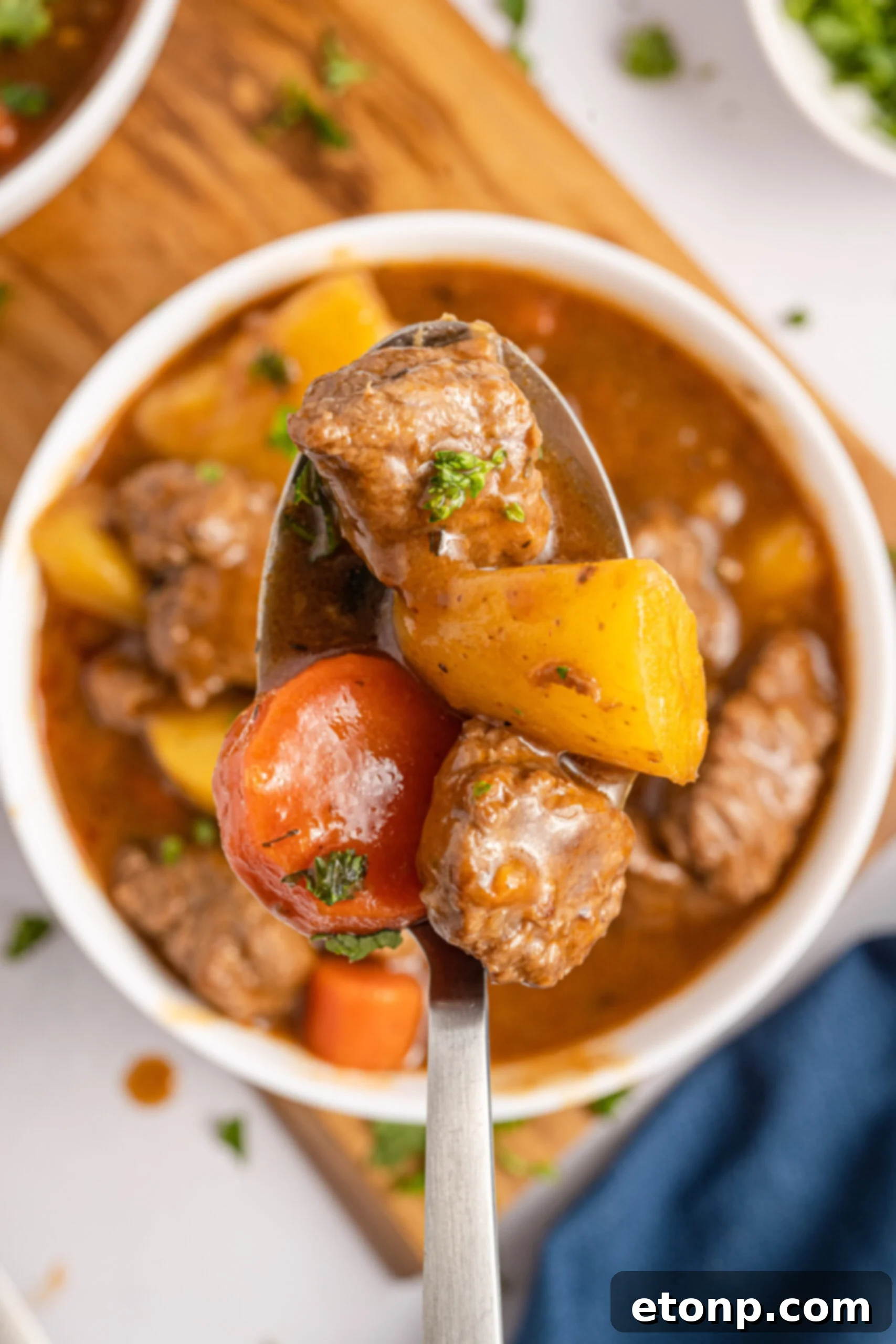 A silver spoon holding Irish Stew over a white bowl of stew. 