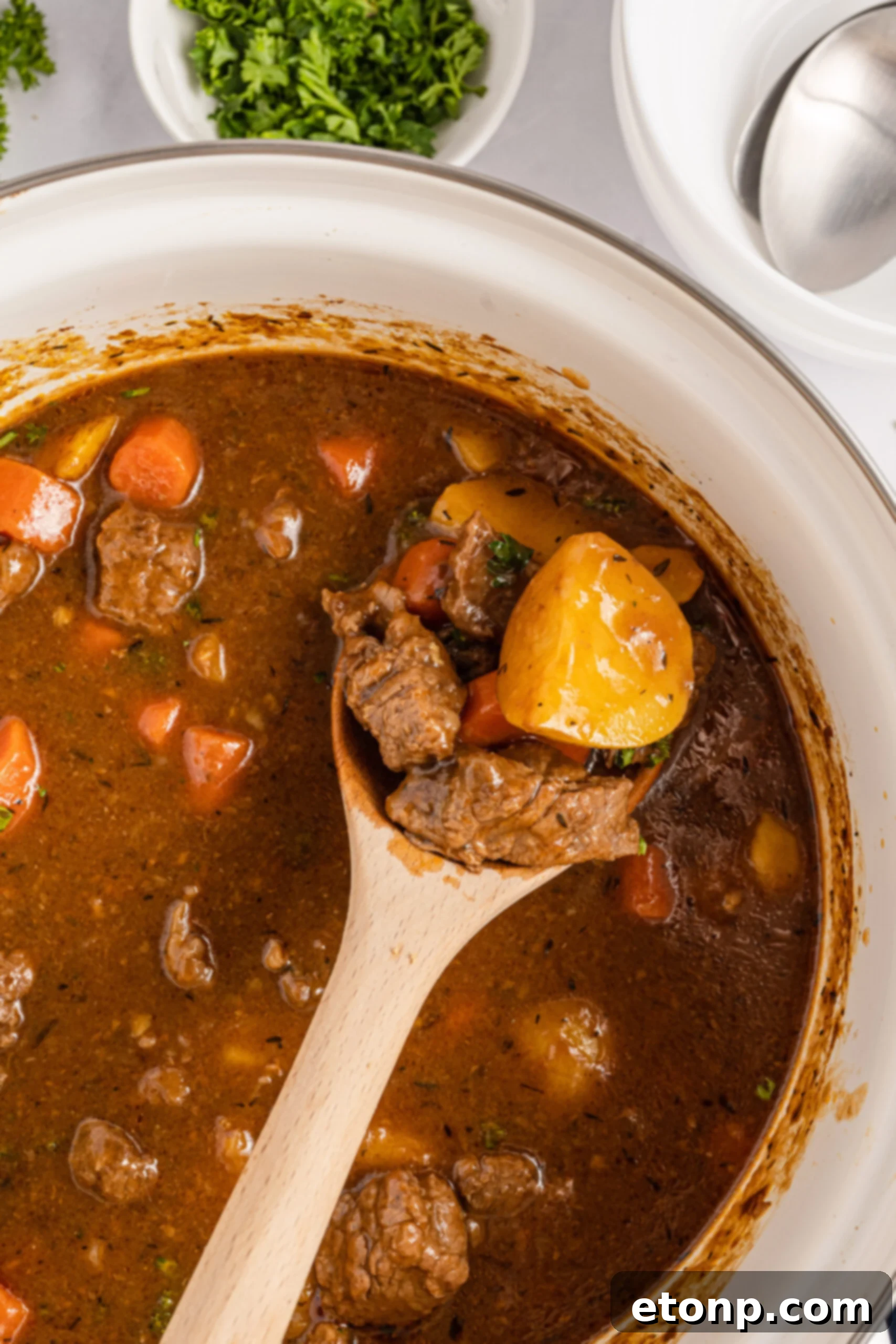  A wooden spoon removing the stew from a large cooking pot. 