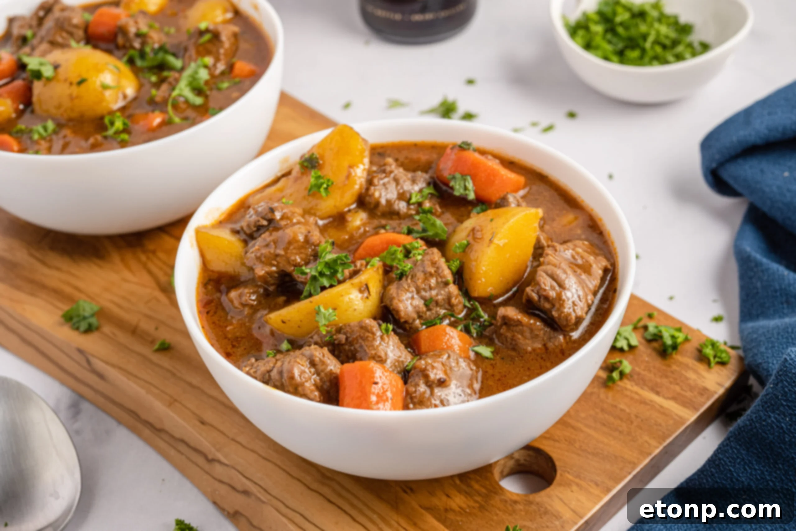 Two bowls of Irish stew sitting on a wooden board with Guinness beer bottles in the background. 