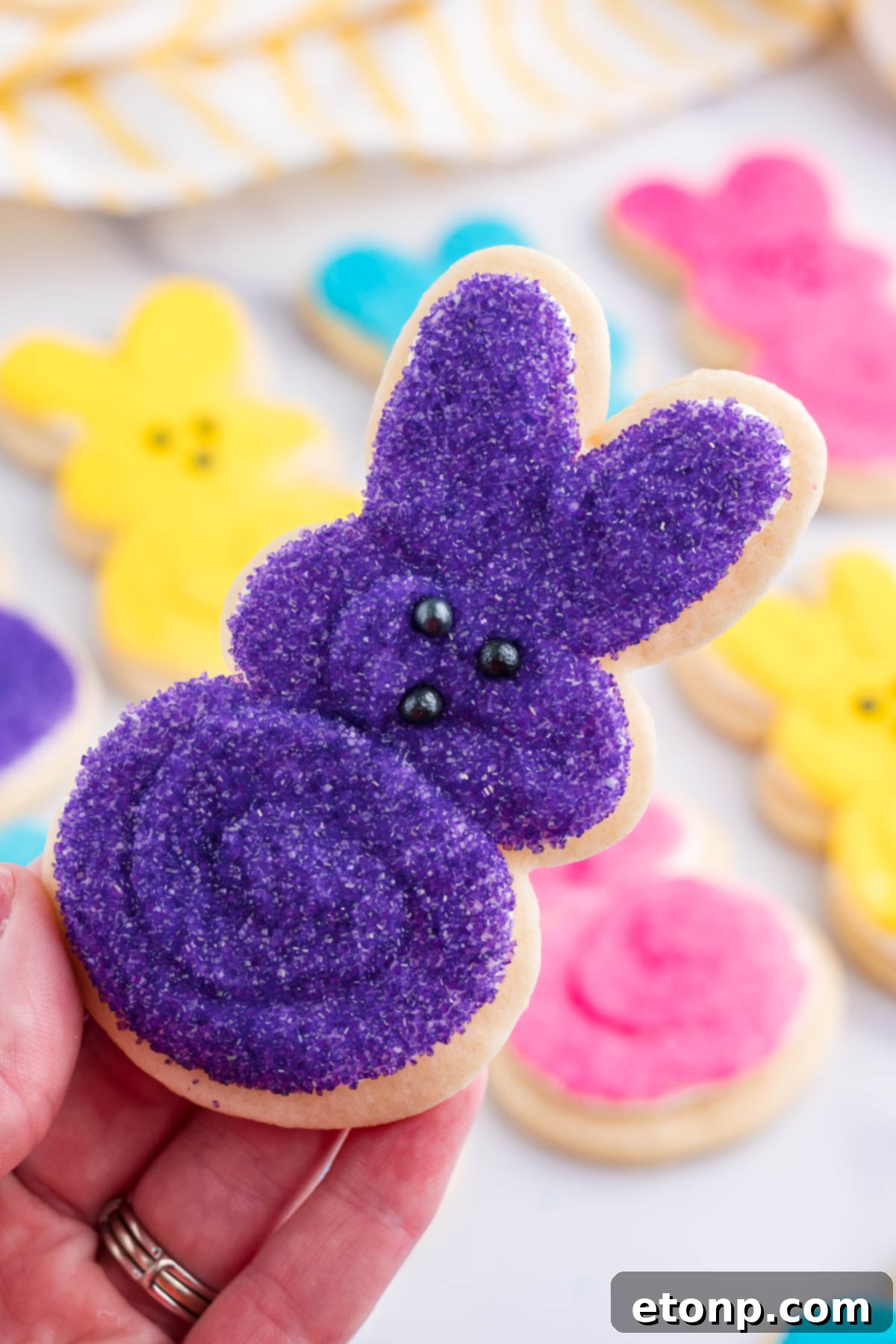 A hand holding up a purple Easter Bunny Cookie. 
