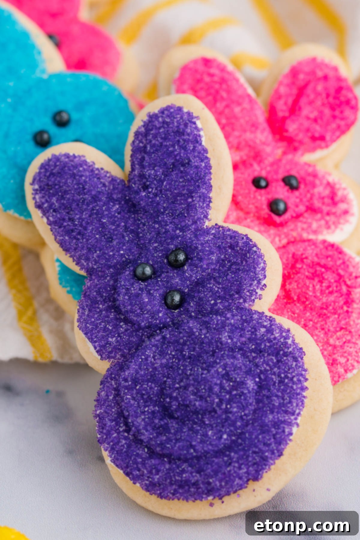 A stack of multicolored Easter Bunny Cookies stacked on a white and yellow linen. 