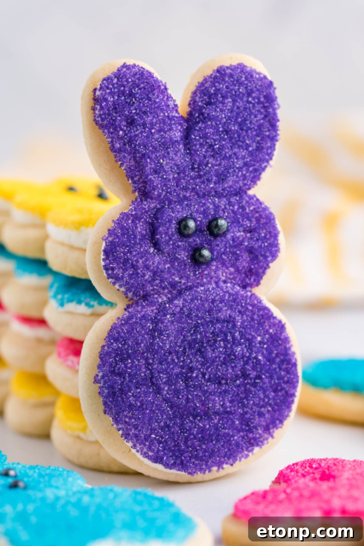A purple Bunny Cookie propped up against a stack of multicolored Easter Bunny Cookies. 