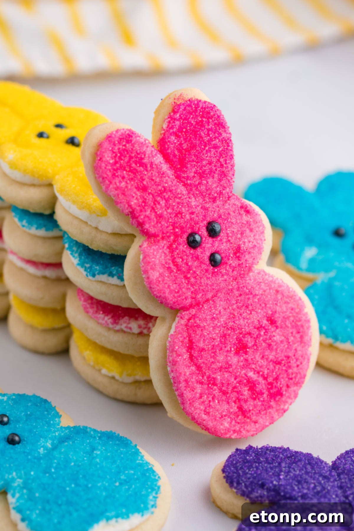 A pink Bunny Cookie propped up against a stack of multicolored Easter Bunny Cookies. 