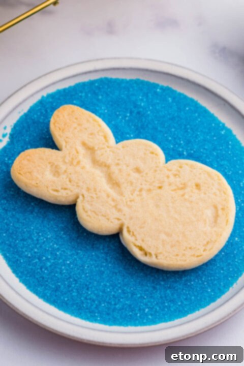 A bunny cookie being dipped in blue sprinkles. 